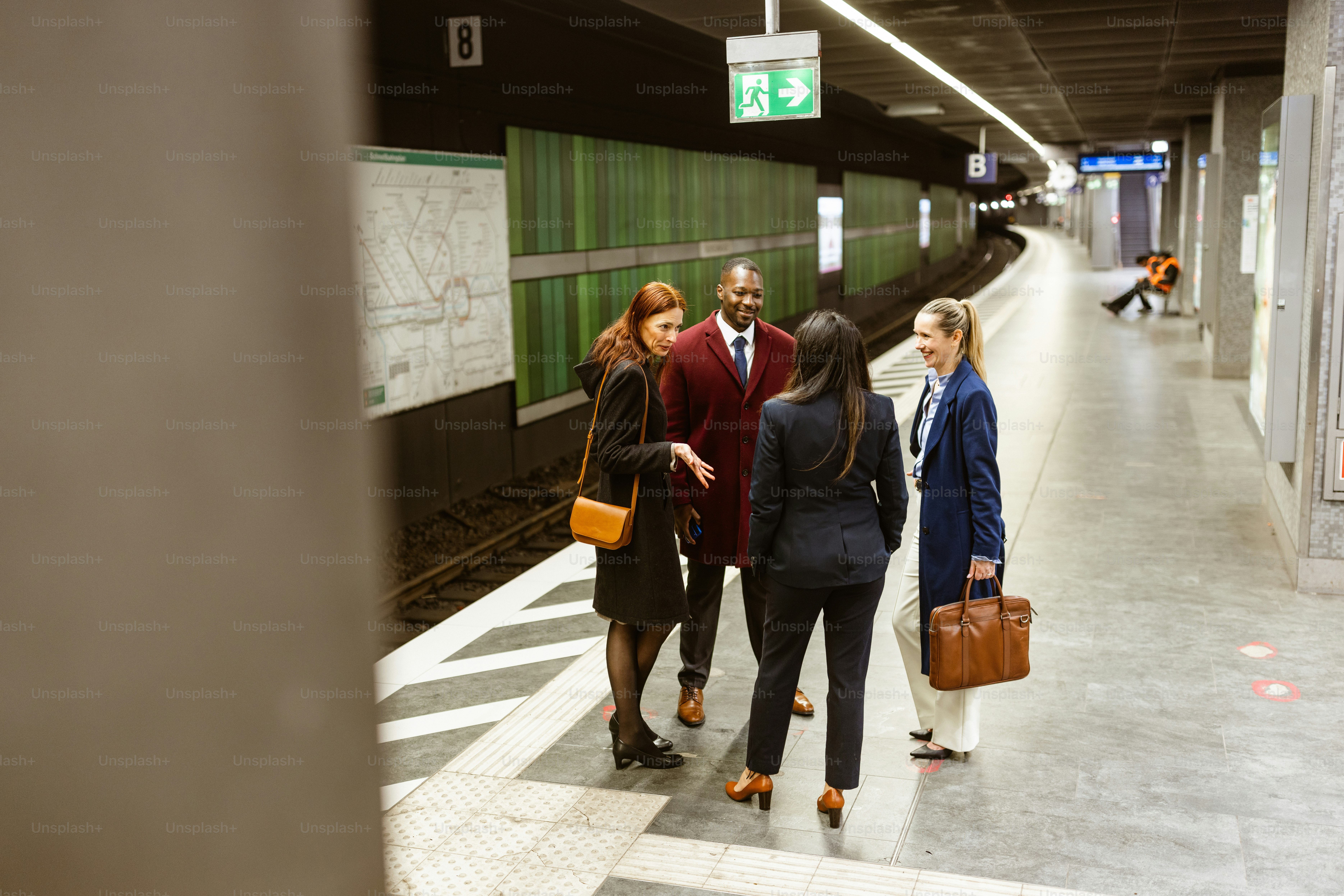A group of four business professionals engaged in conversation while waiting for the subway on an early morning. The platform is relatively empty
