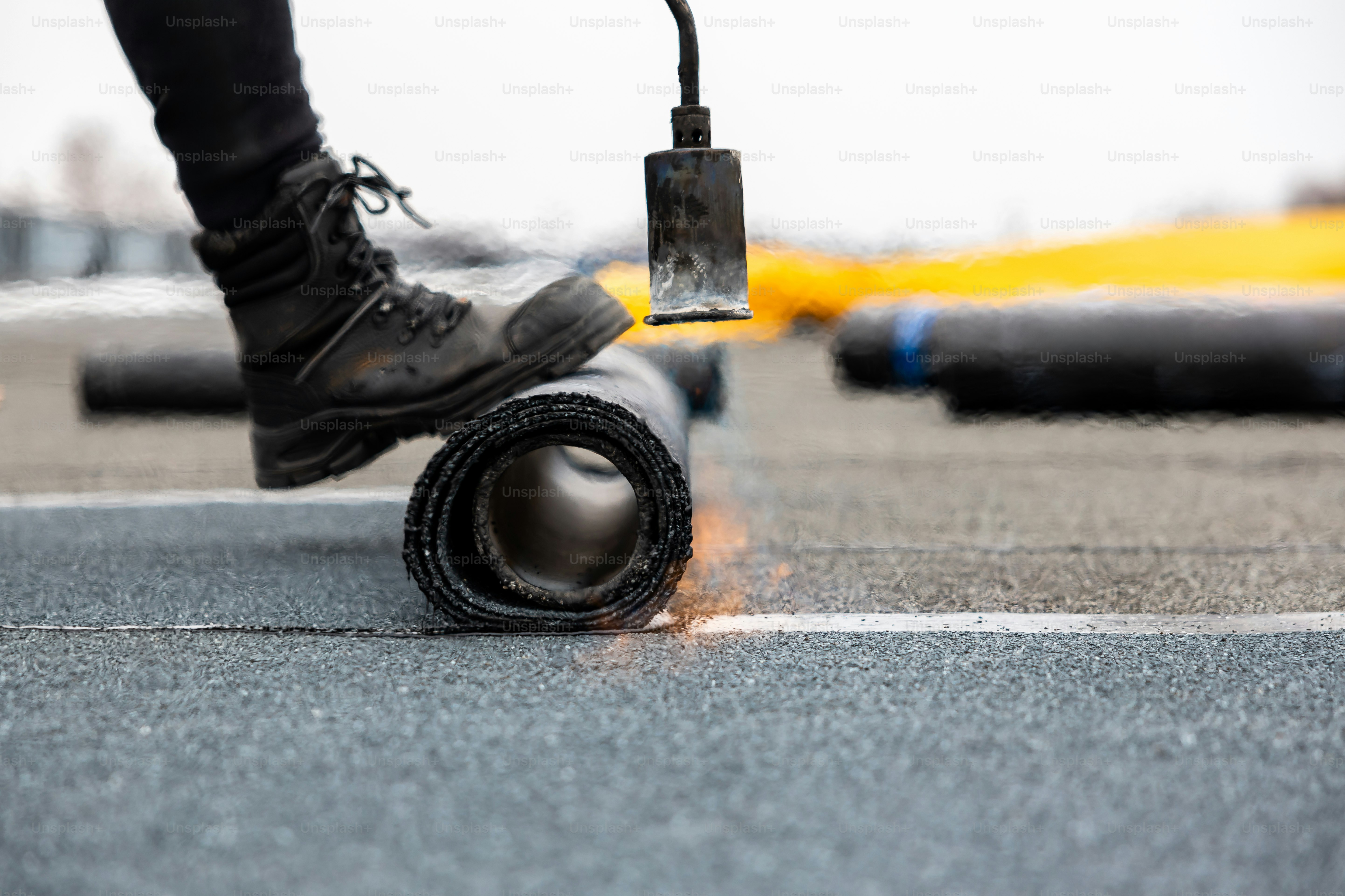 professional roofer at work securing rolled tar paper with a blowtorch on a flat roof installation process