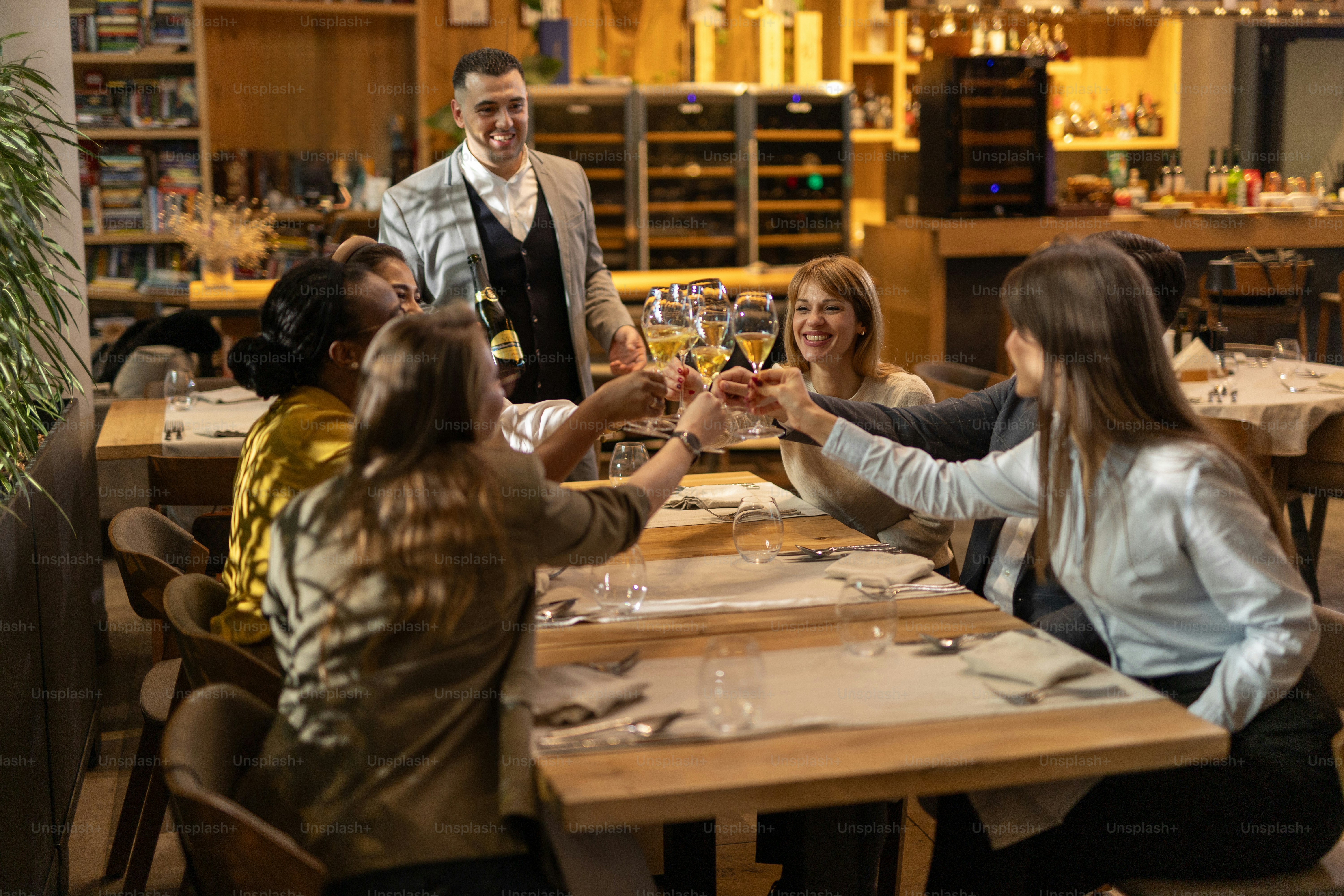Cheerful multiracial group of guests toasting with white wine in luxury restaurant