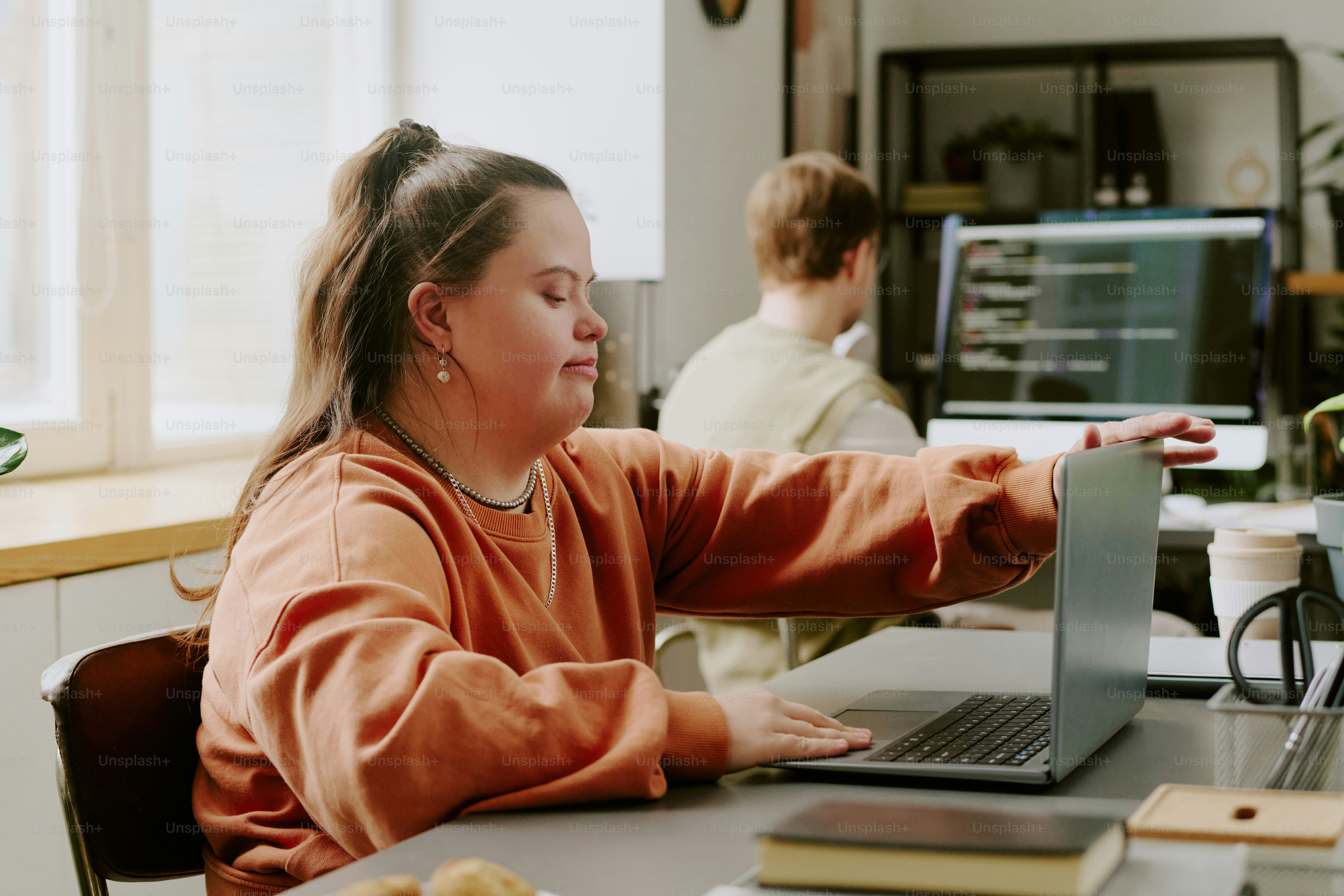 Bidikan sedang programmer dengan sindrom down membuka laptop saat bekerja di kantor yang diterangi oleh sinar matahari