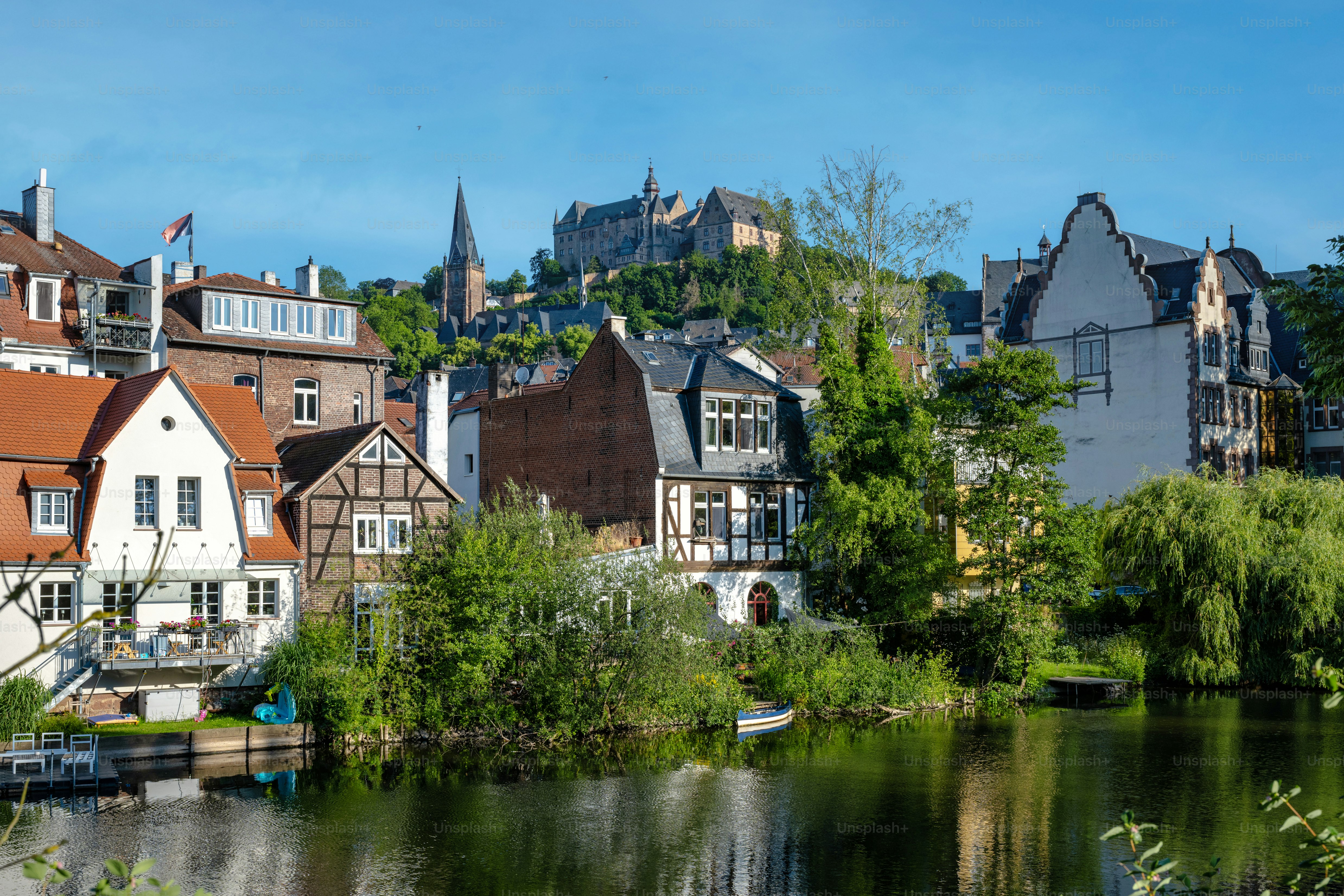Blick auf das historische Marburg über die Lahn bei blauem Sommermorgen mit Wehr im Vordergrund und Schloss im Hintergrund