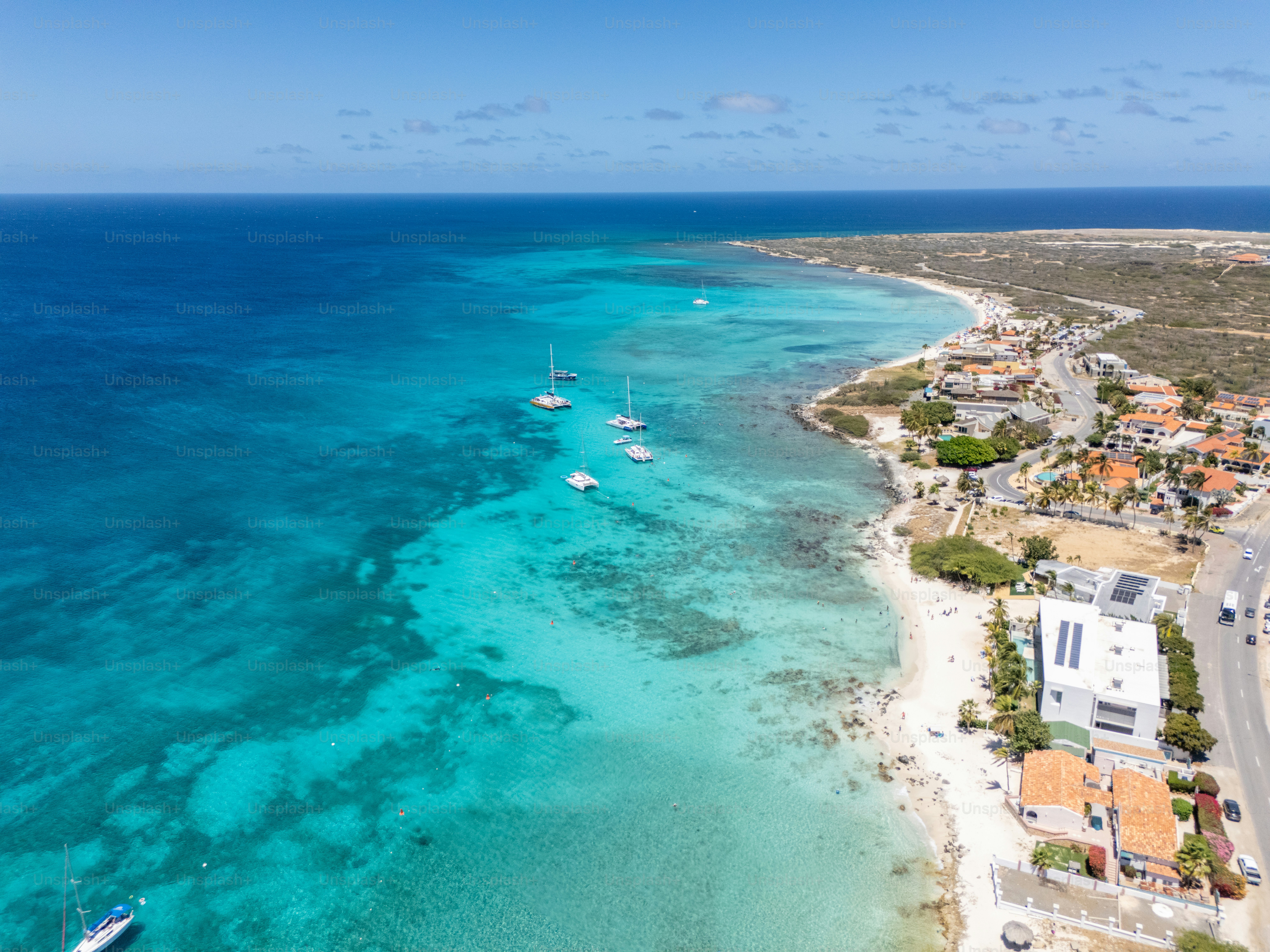 Stunning aerial shot of rocky coastline with clear blue sea and anchored boats. Coastal road winding along the shoreline. Idyllic beach scene for travel and tourism enthusiasts.