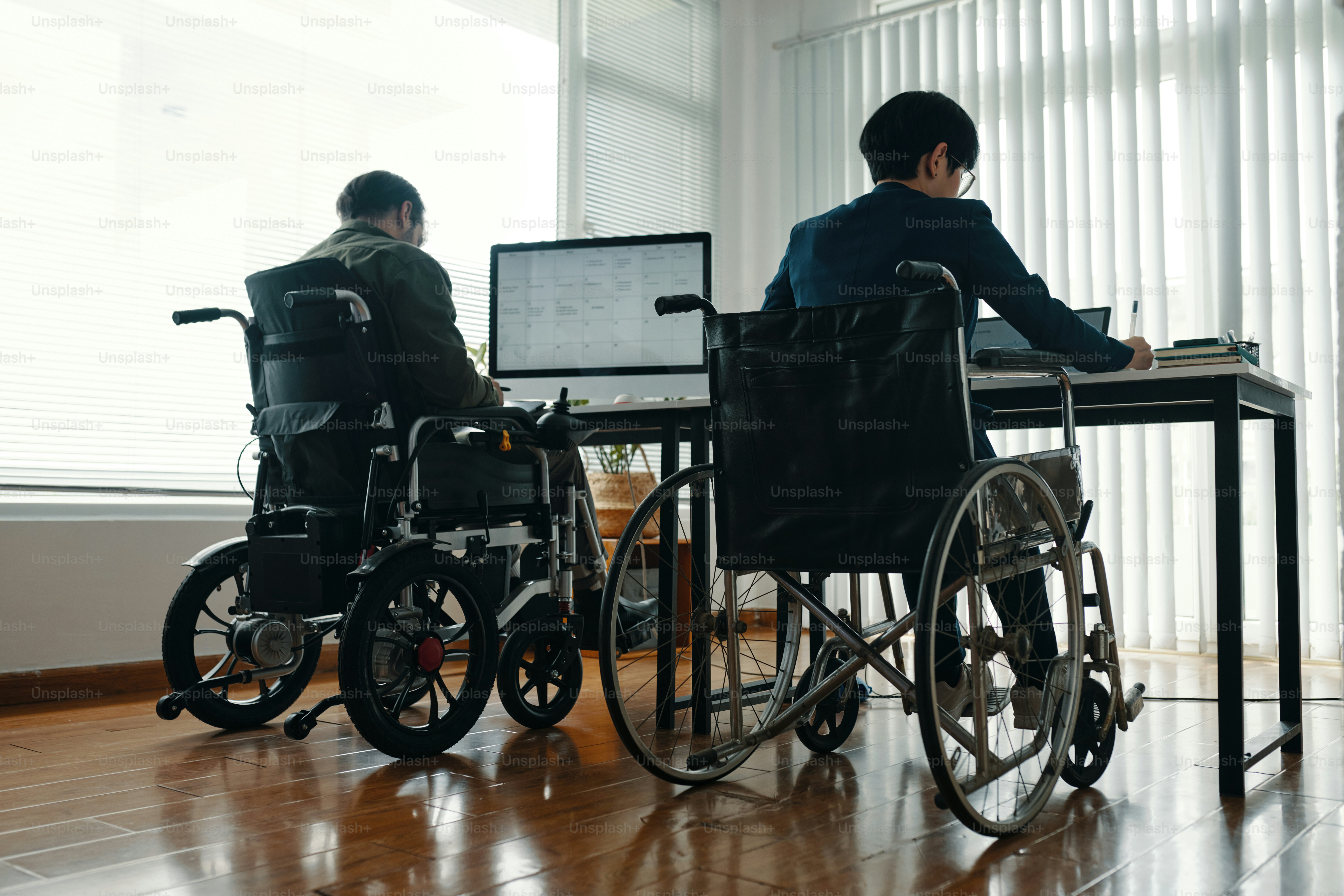 Tampilan belakang rekan kerja penyandang disabilitas duduk di kursi roda dan bekerja di komputer