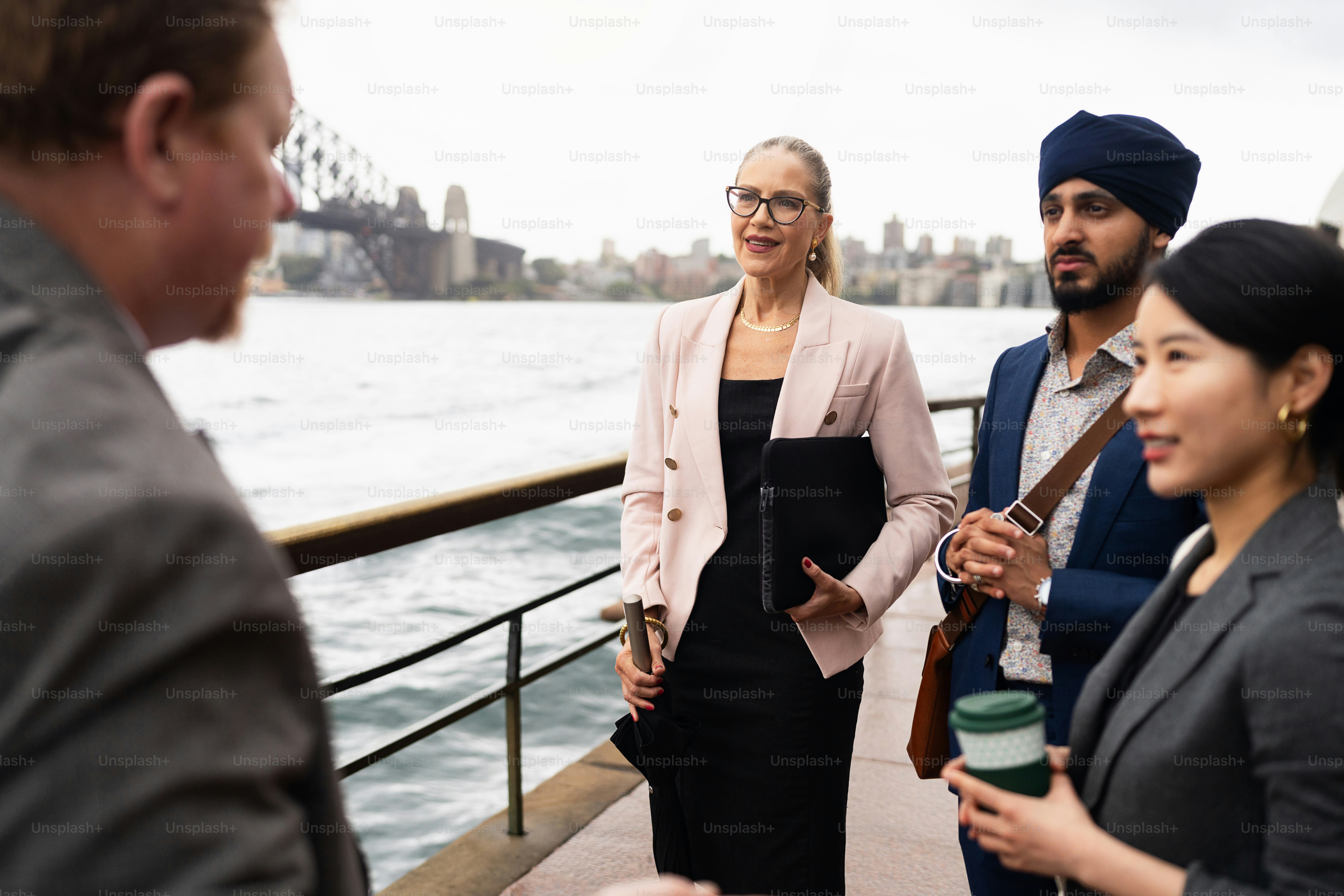 A diverse group of business professionals socialize outdoors, near iconic Sydney landmarks, fostering connections and collaboration.