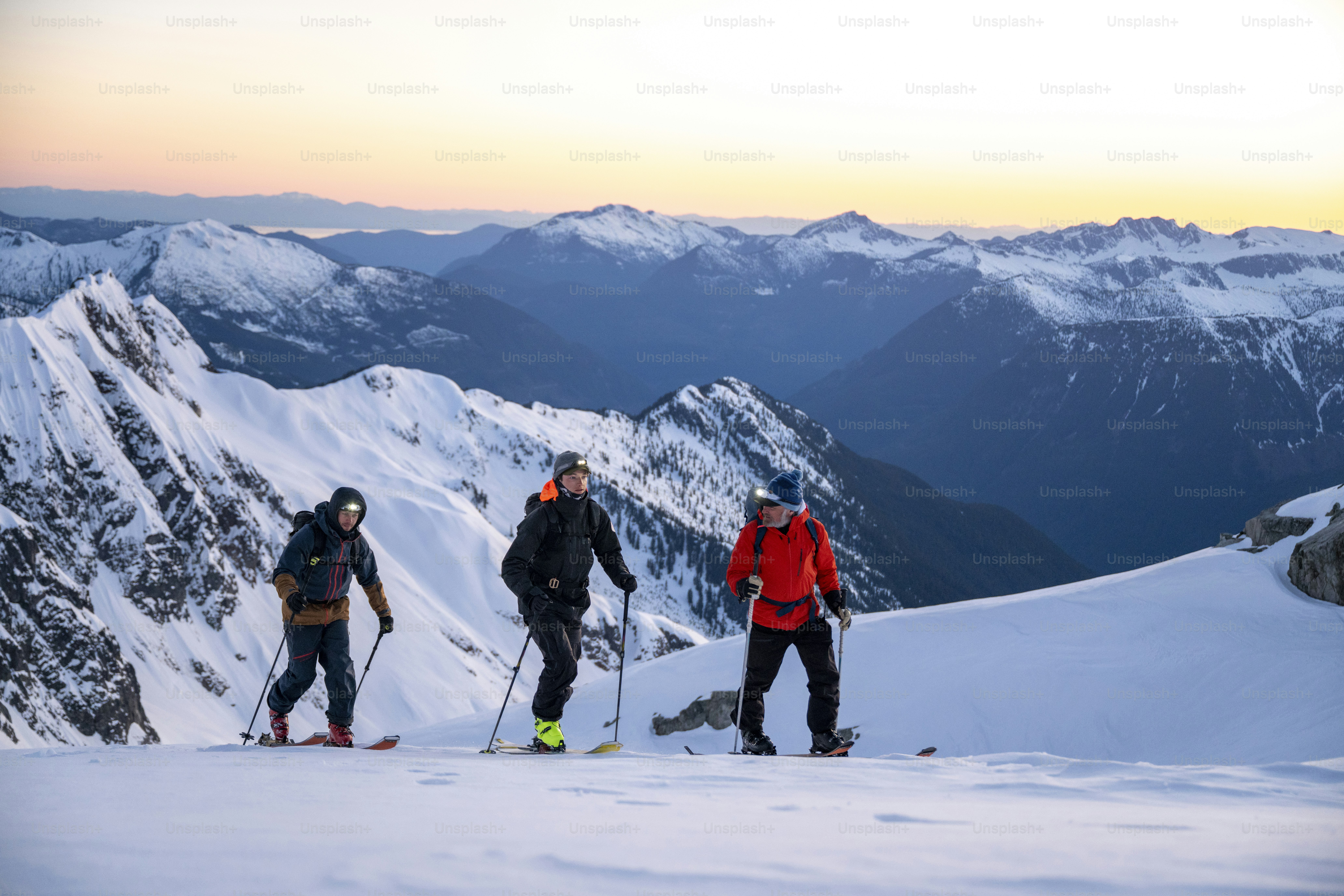 Los esquiadores de travesía ascienden a la montaña nevada al amanecer con linternas frontales, Cordillera Tantalus, Columbia Británica.