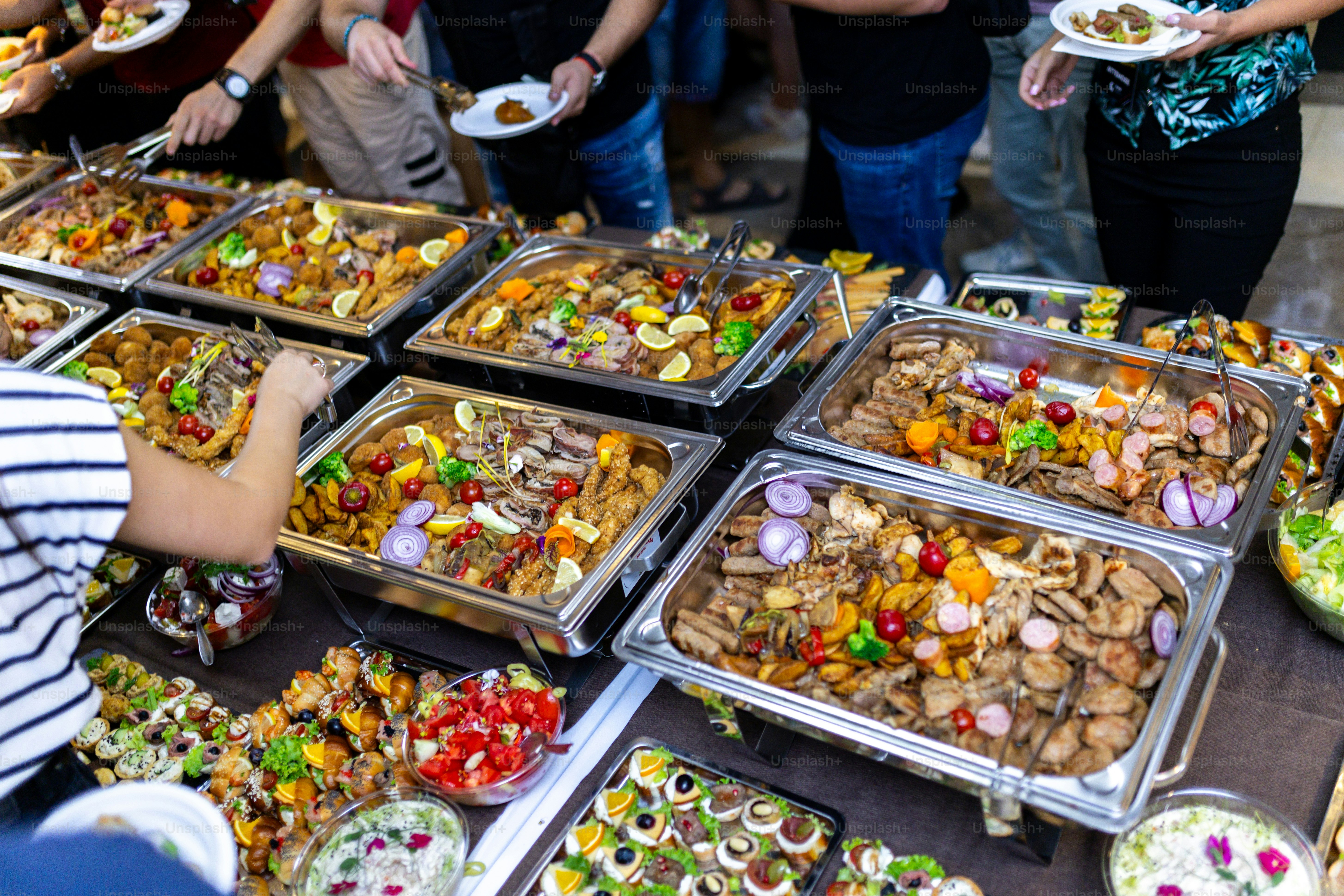 A vibrant buffet display features an array of colorful dishes, including meats, salads, and desserts, as guests are seen filling their plates at a lively gathering.
