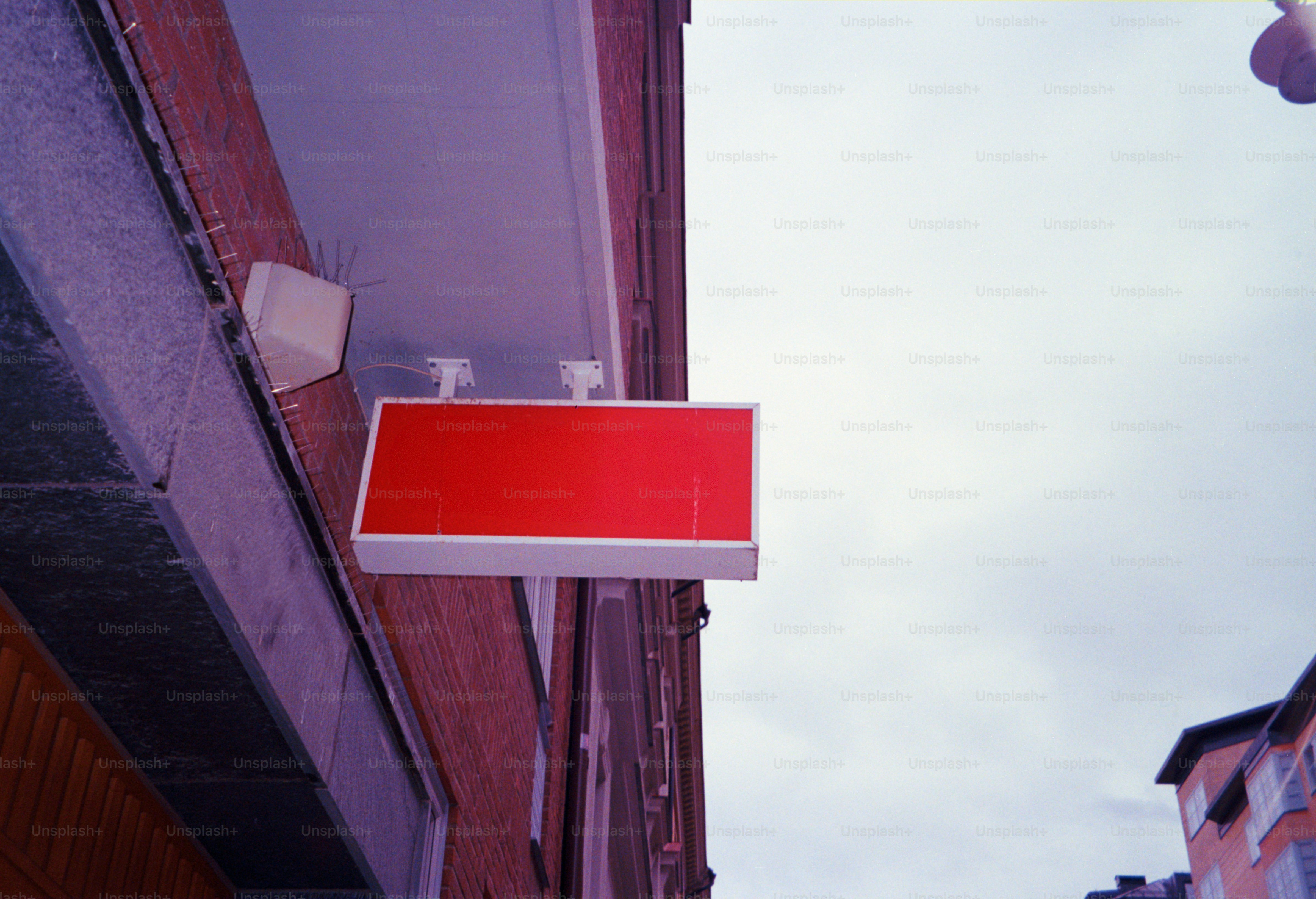 A blank red sign hangs on a brick building.