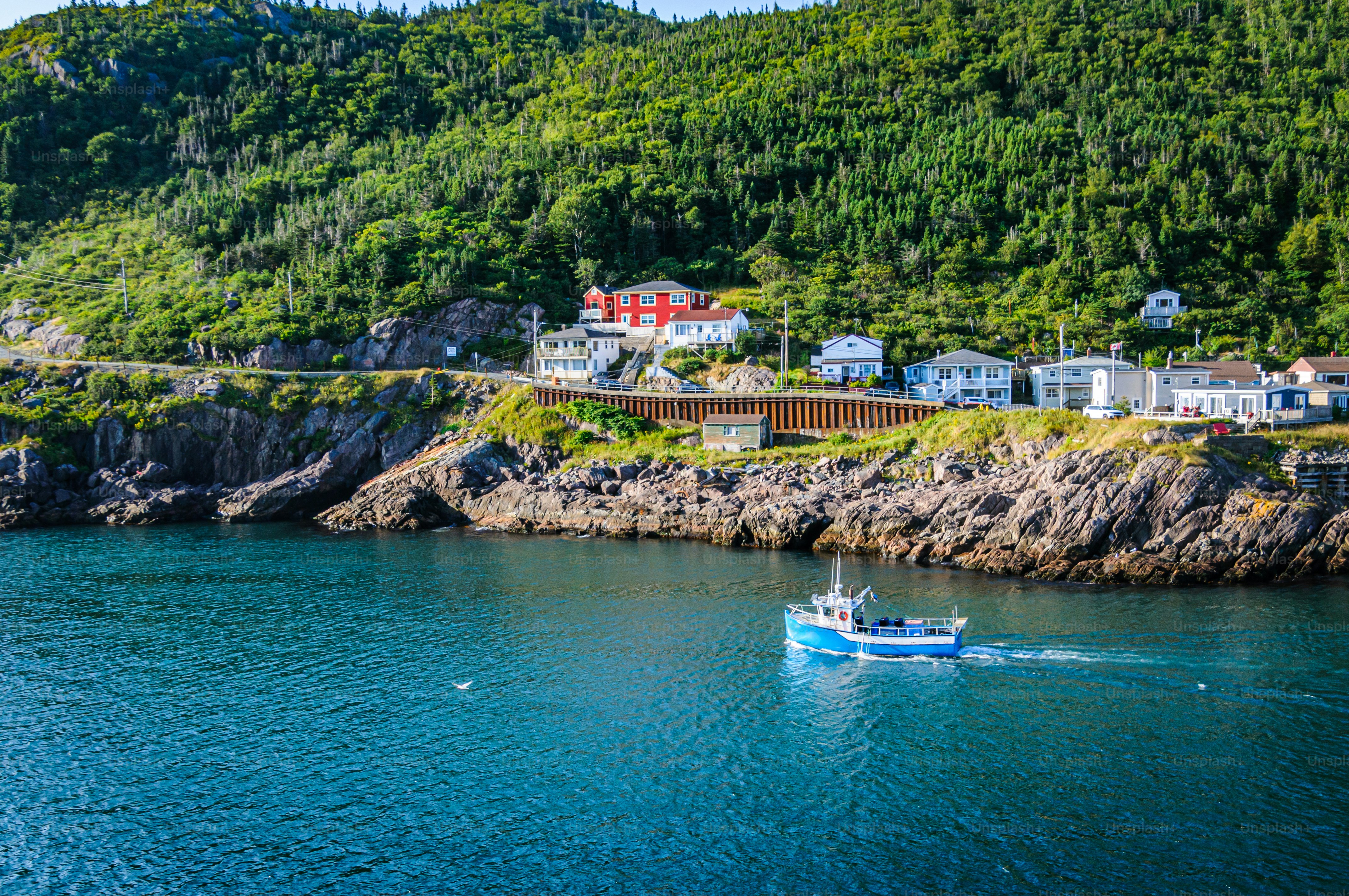 A blue fishing trawler  passes a row of homes  in The Narrows Channel leading to St. John's Harbor in Newfoundland