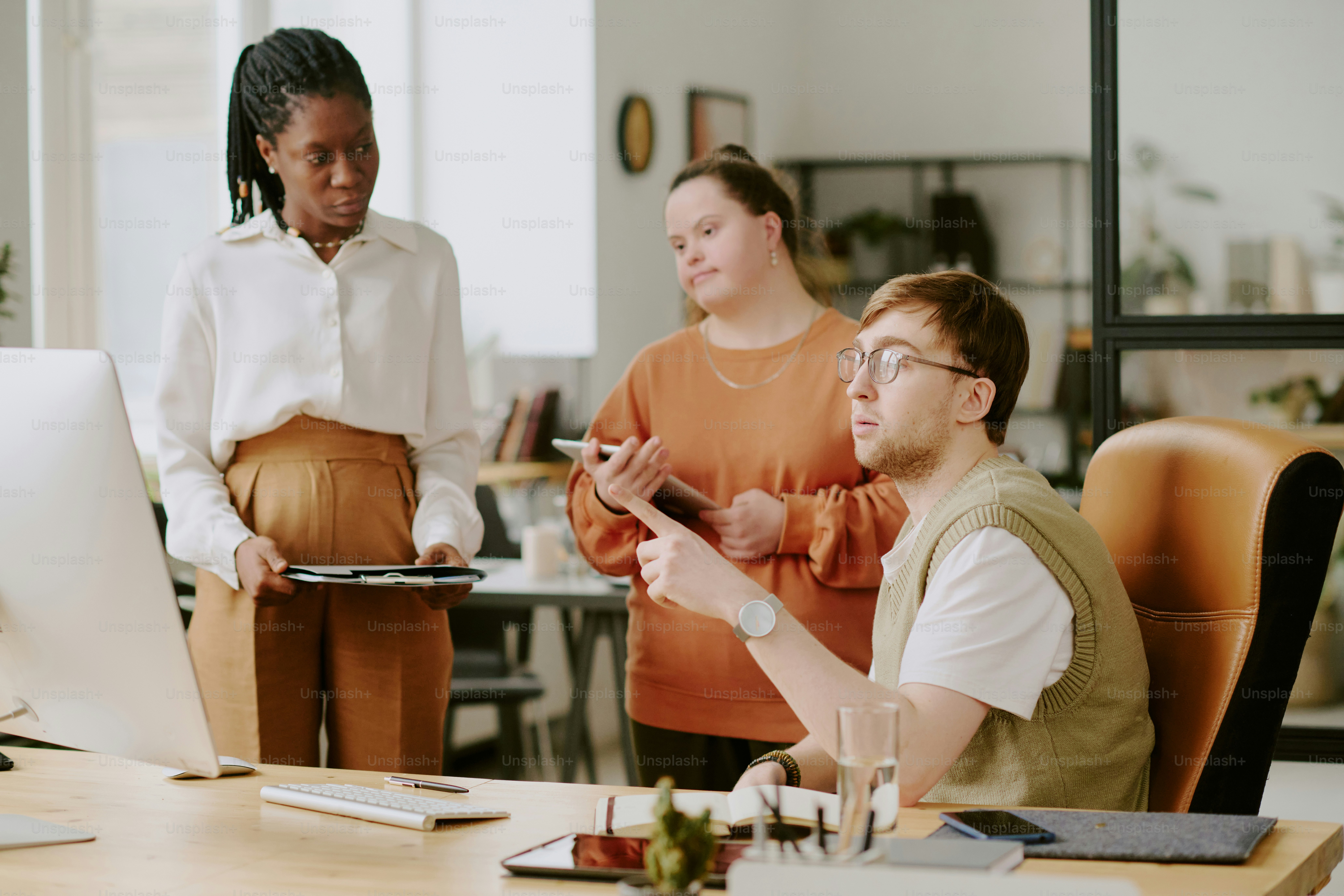 Medium shot of biracial team of developers looking at screen of computer while discussing work plans