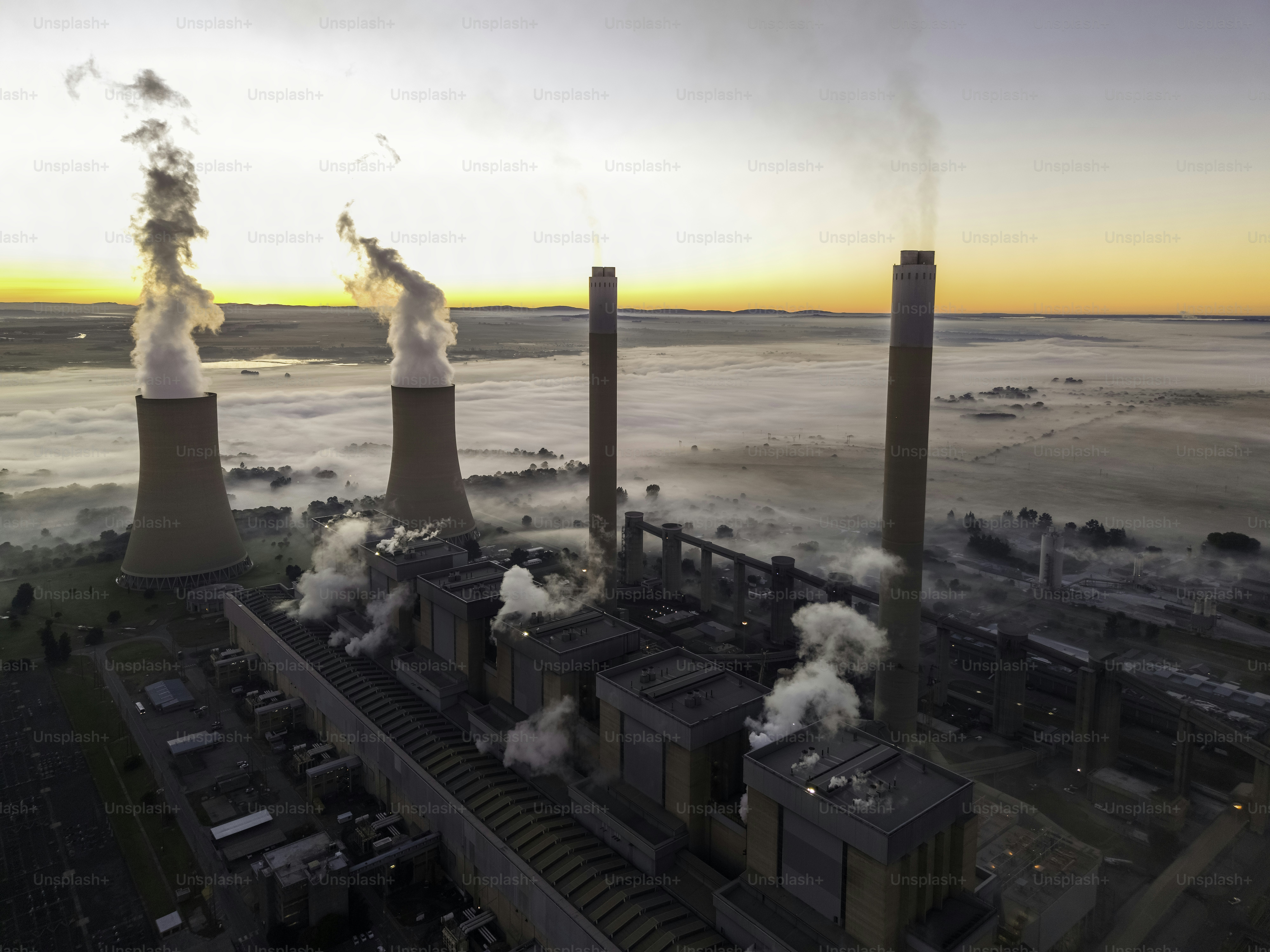 Usina de energia de Lethabo vista ao nascer do sol com a poluição e a névoa sobre o campo e o vapor subindo das torres de resfriamento.