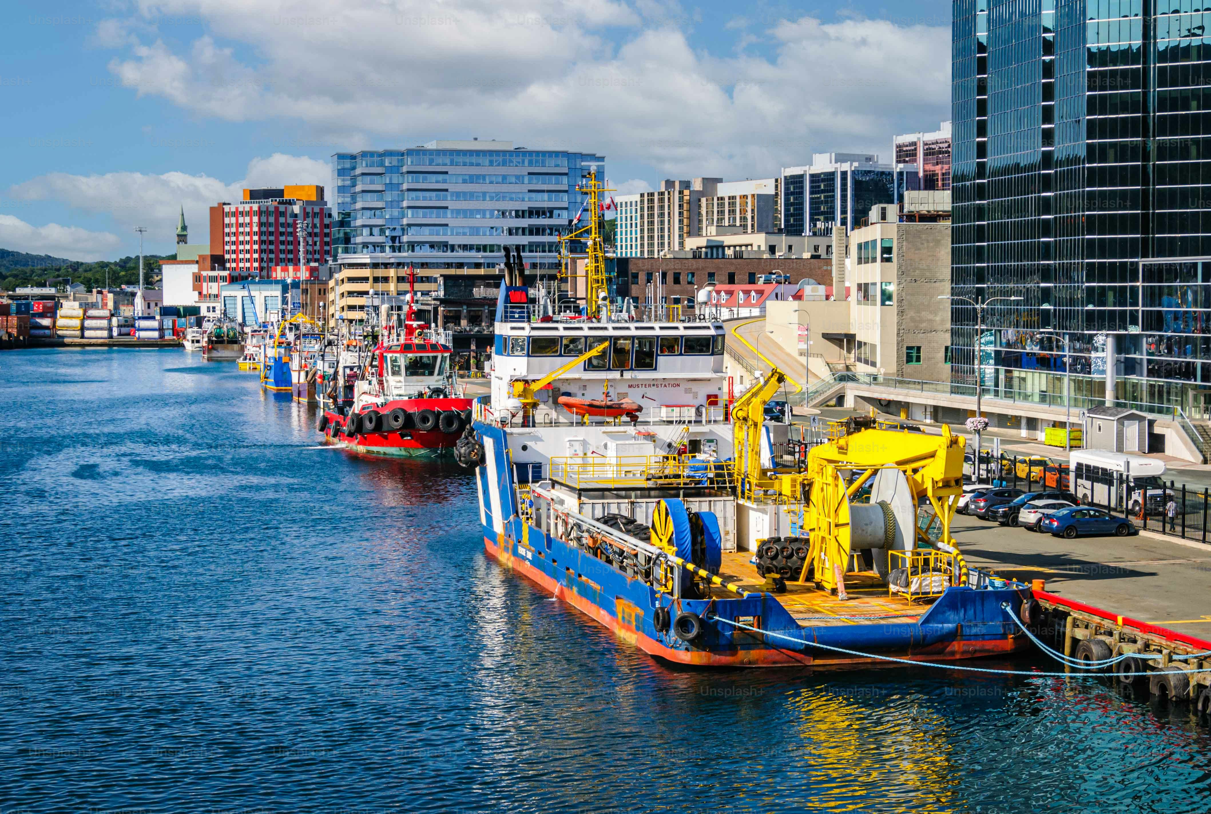 A row of colorful industrial ships find dockage along the pier of St. John's on a Sunday morning across from modern glass office buildings.