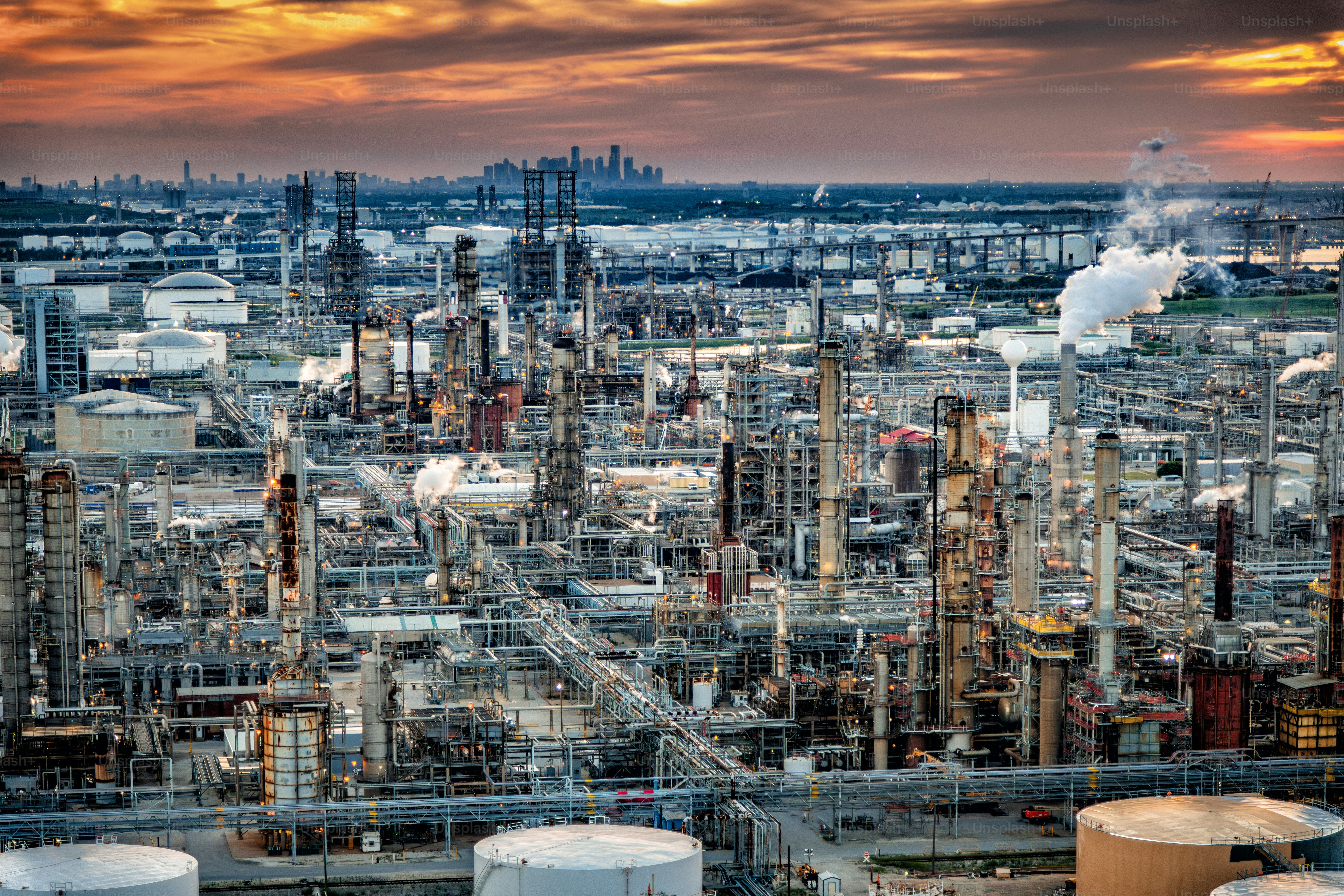 Vista aérea de uma grande refinaria localizada nos arredores de Houston, Texas, filmada de helicóptero de uma altitude de cerca de 500 pés com o horizonte da cidade ao longo do horizonte.