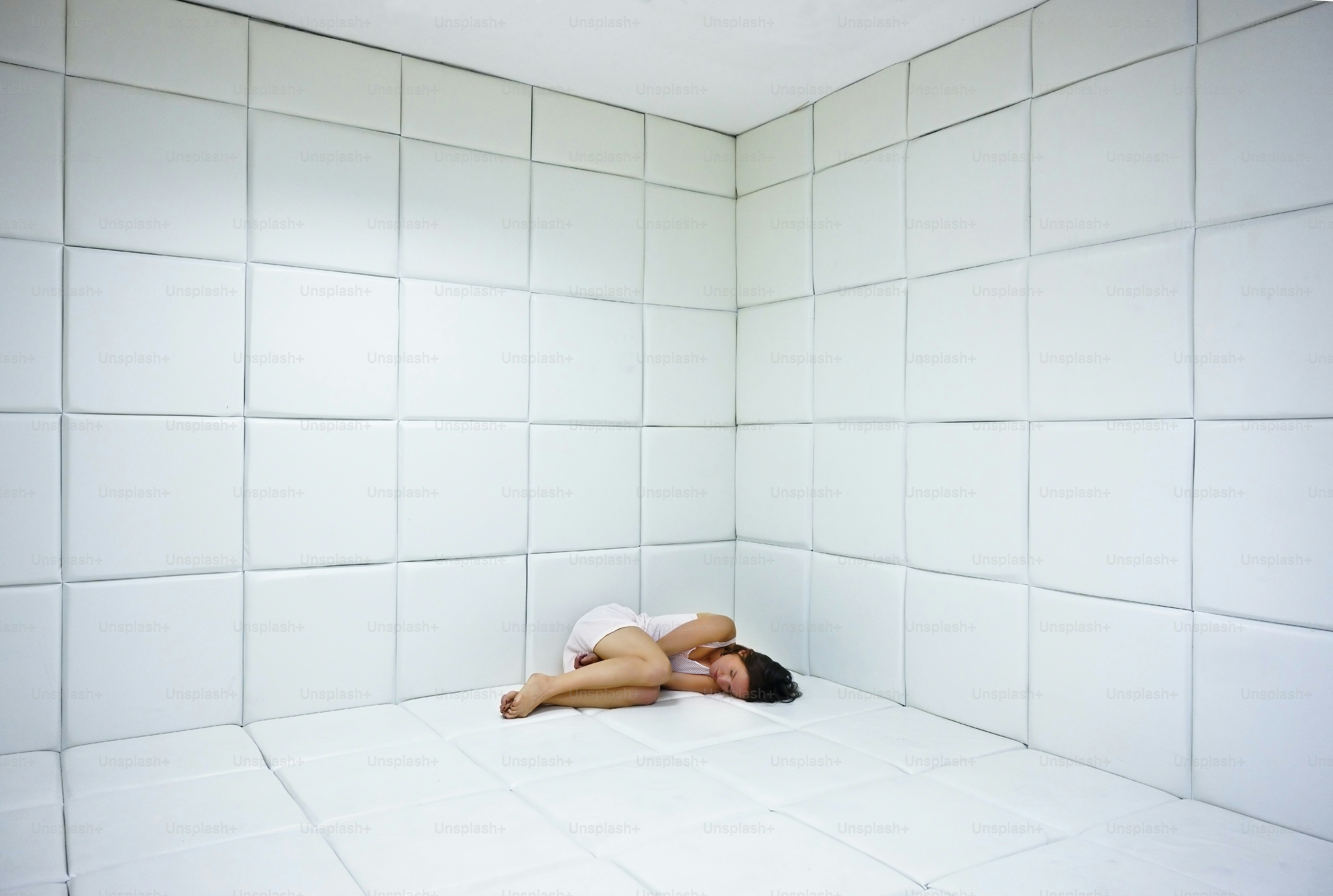 精神病院の白いパッド入りの部屋の床に横たわる白衣を着た若い女性」n