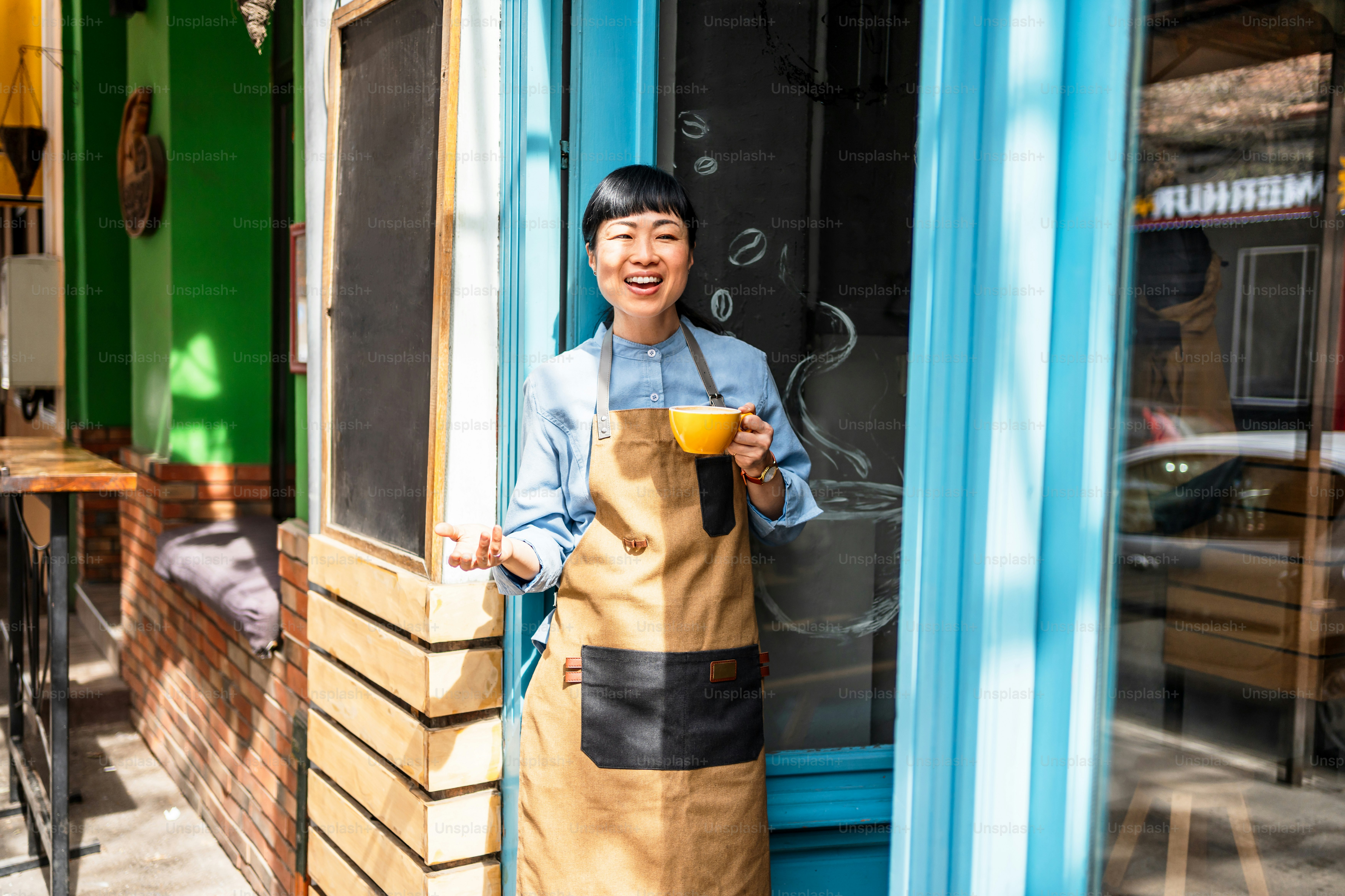 Propriétaire de café joyeux debout à l’entrée de leur magasin, tenant une tasse de café et souriant. Atmosphère lumineuse et accueillante avec des couleurs vives et une ambiance accueillante