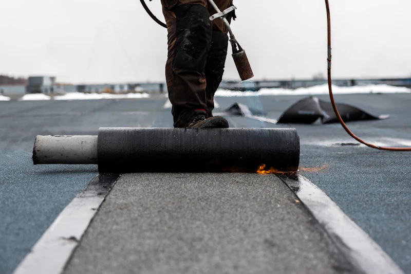 Roofer torch-welding a membrane on a flat commercial roof
