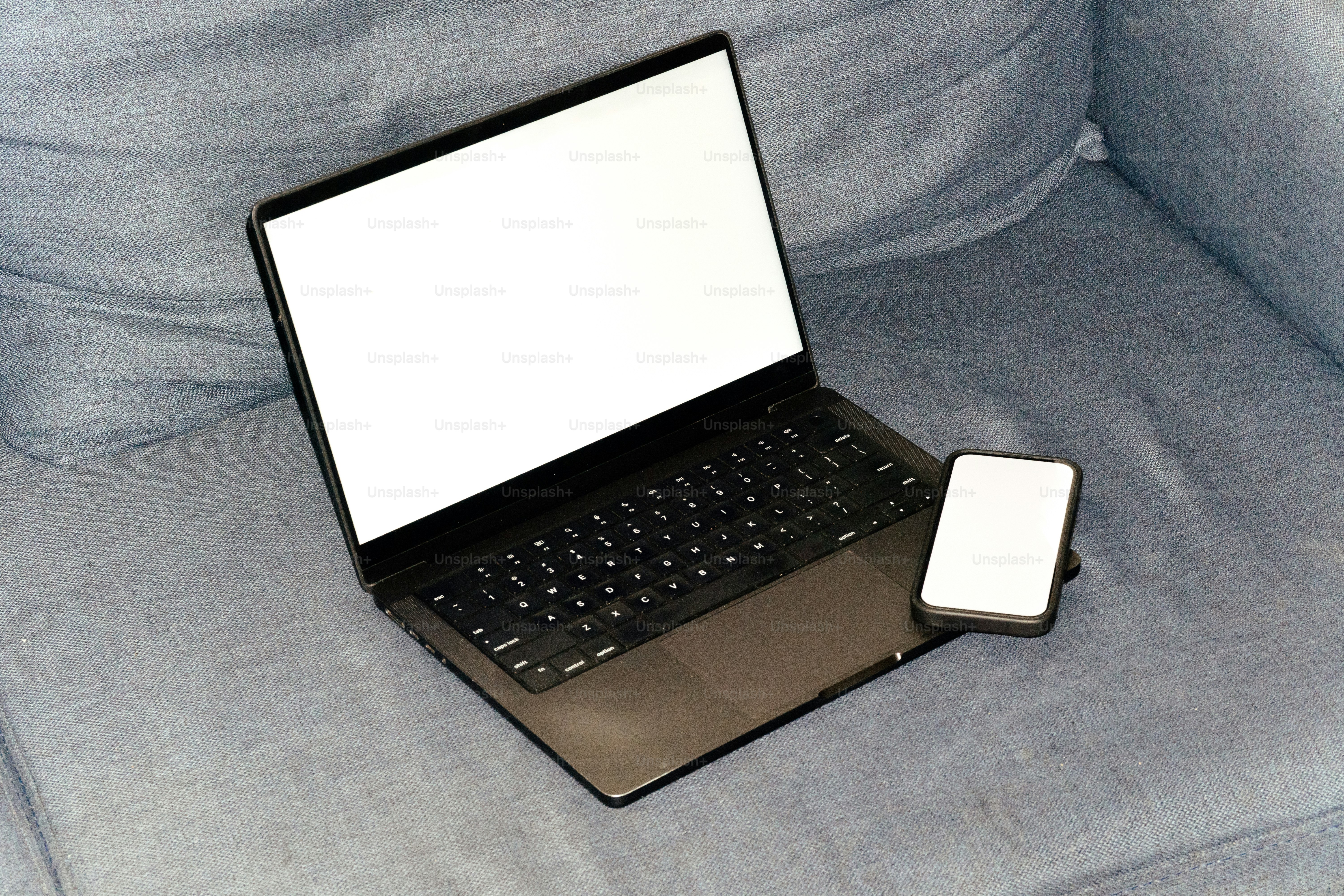 Laptop and phone are on a blue couch.