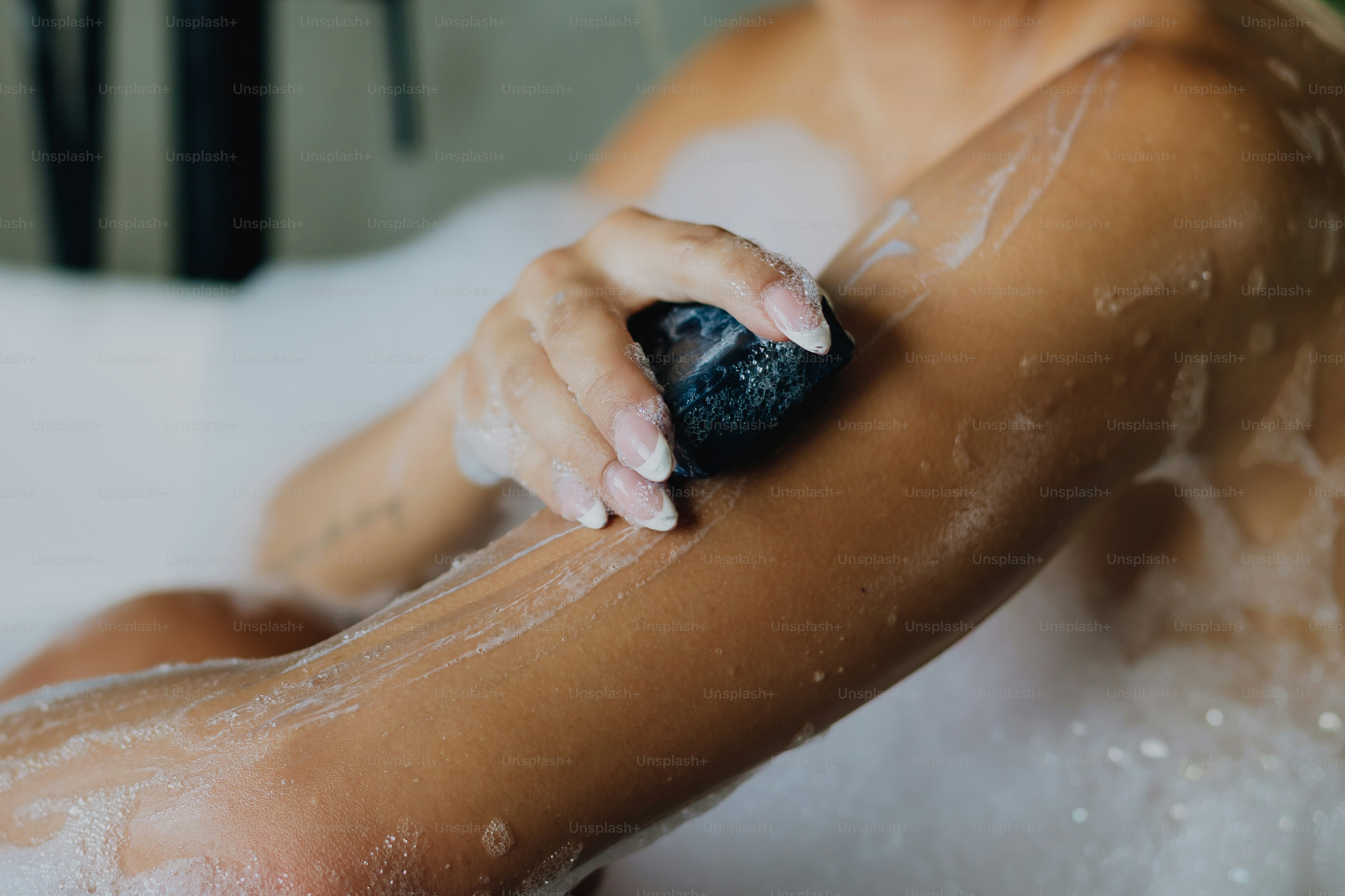 Woman washing arm with a bar of soap in bubbly bath
