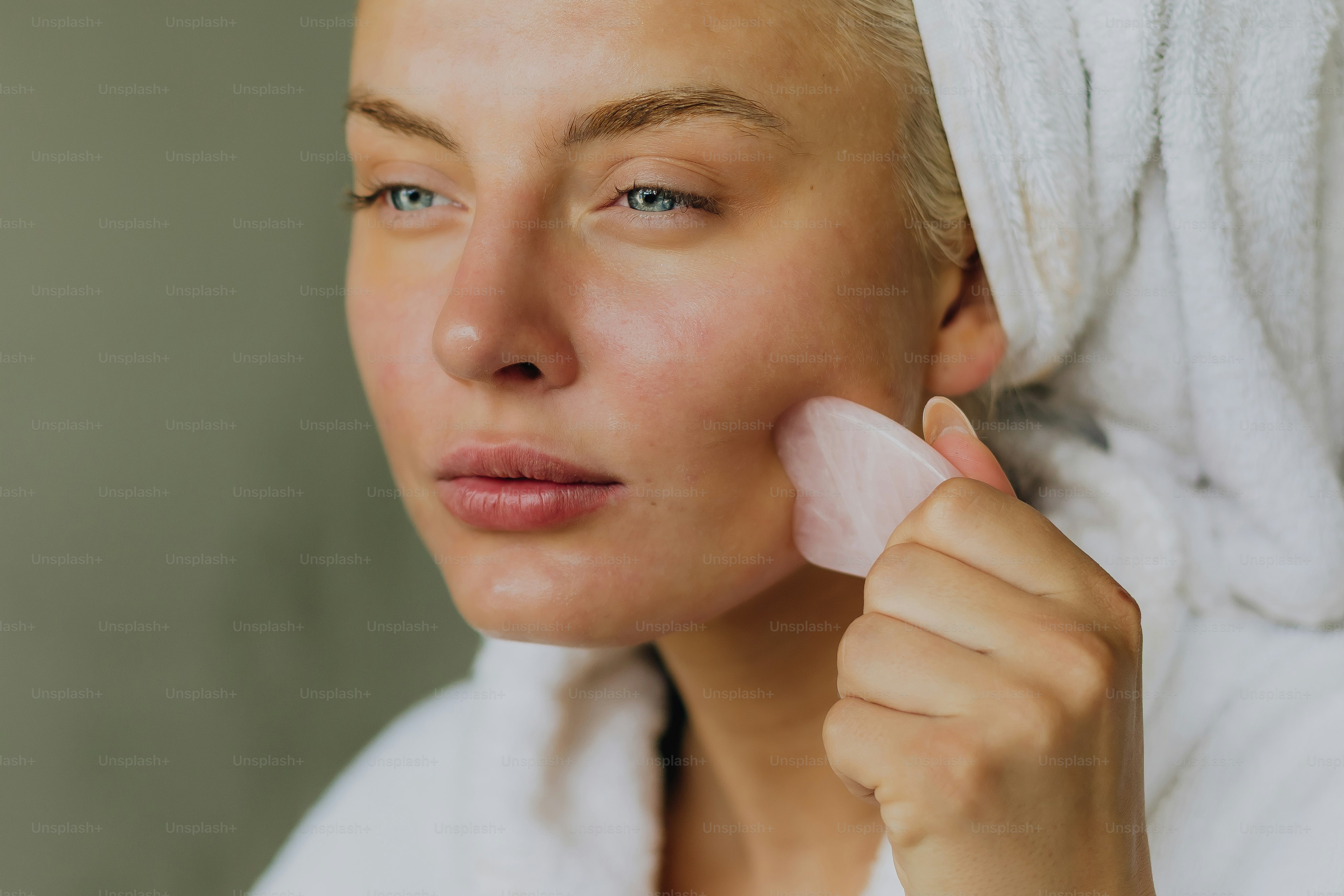 Woman using a pink gua sha tool on her face