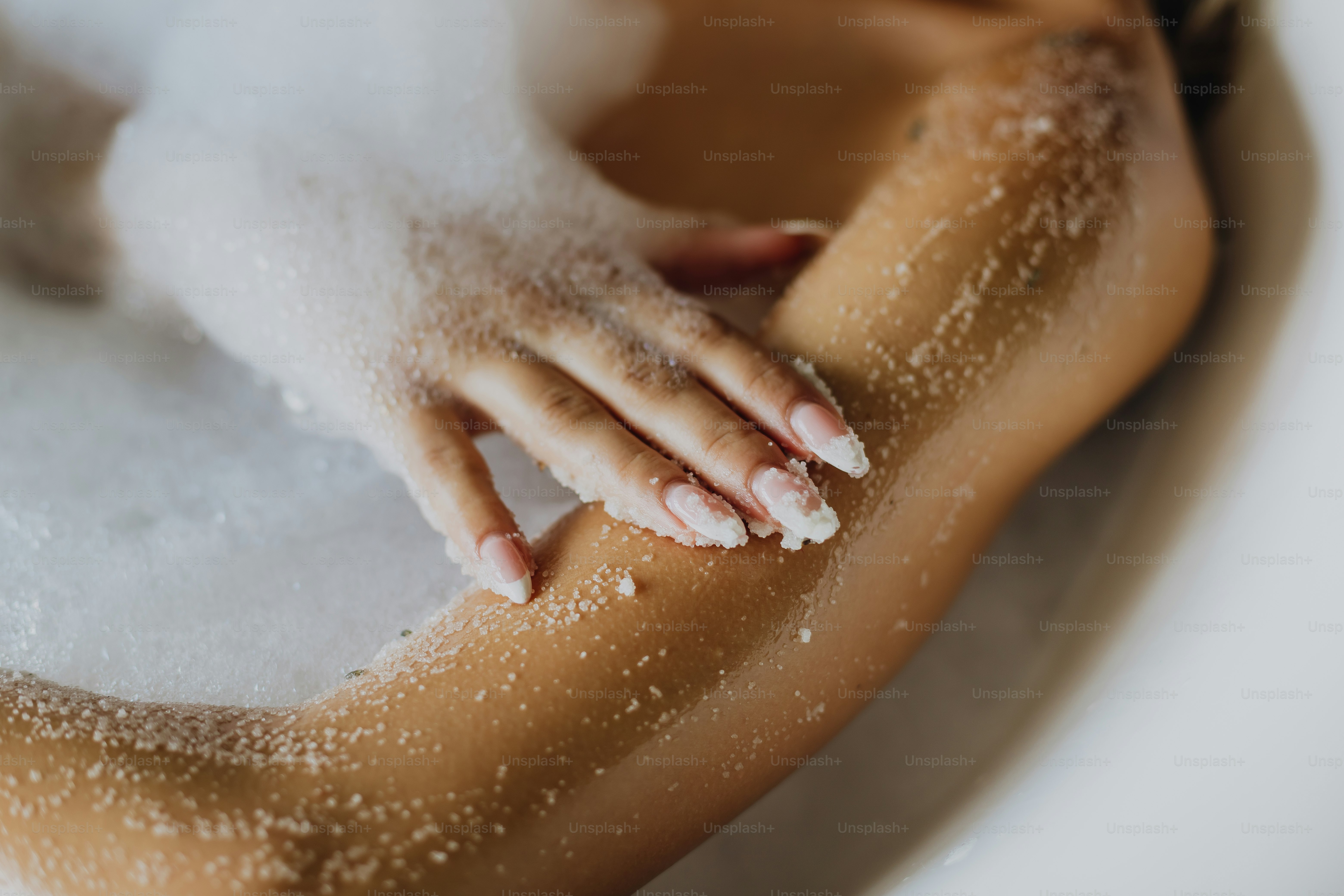Woman applying body scrub in a bubble bath