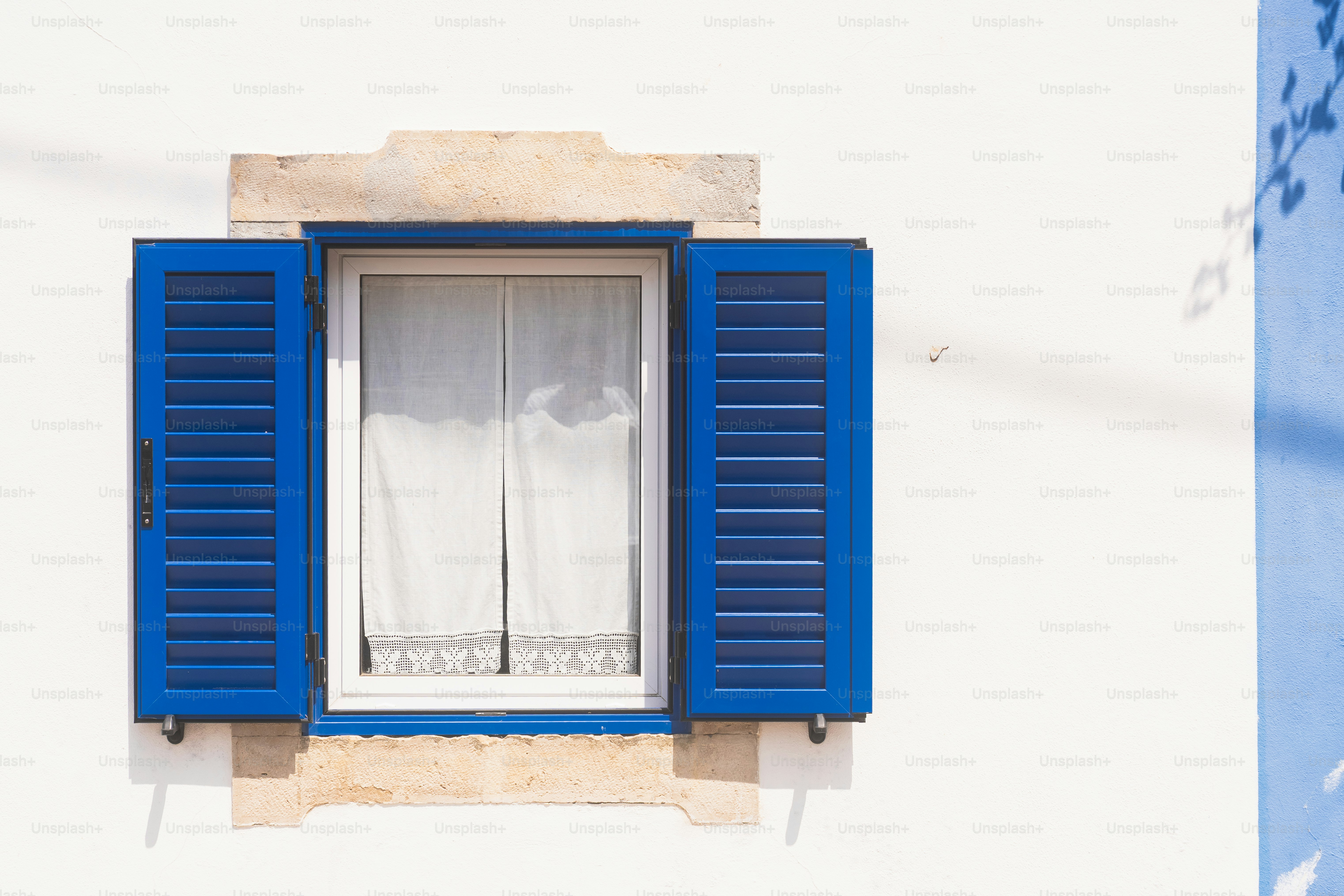 White window with open blue shutters on wall