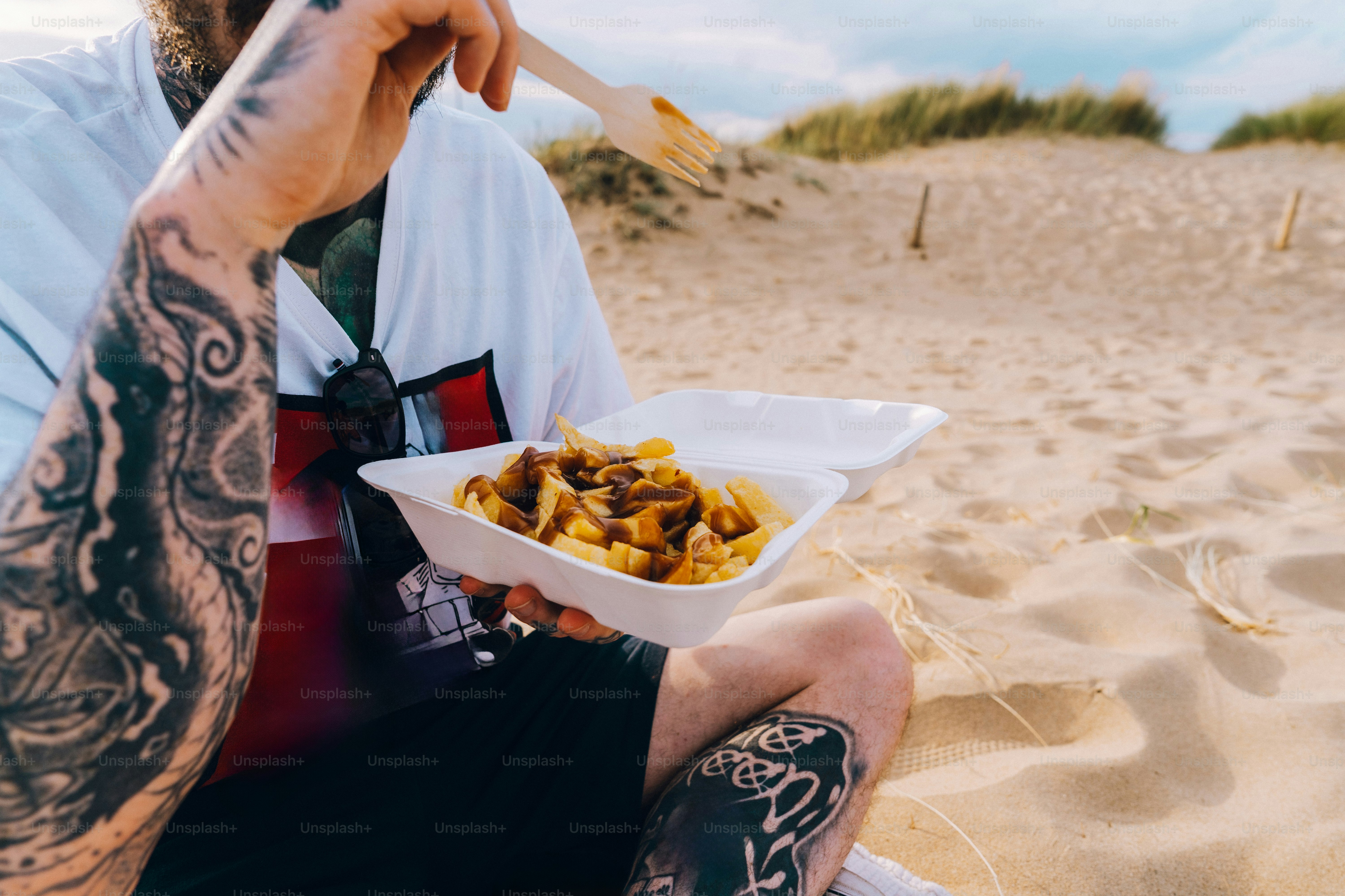 Person with tattoos eating fries on the beach