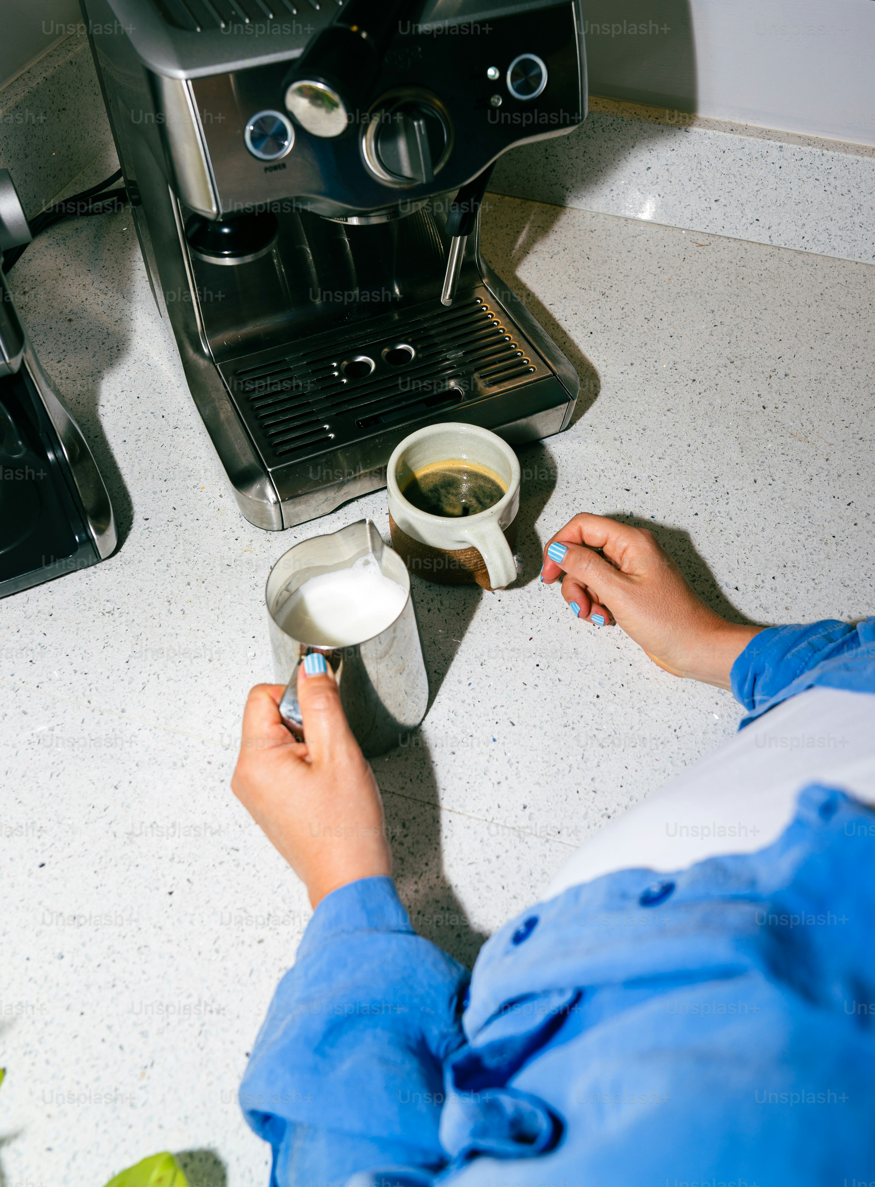 Person making coffee with espresso machine and milk pitcher.