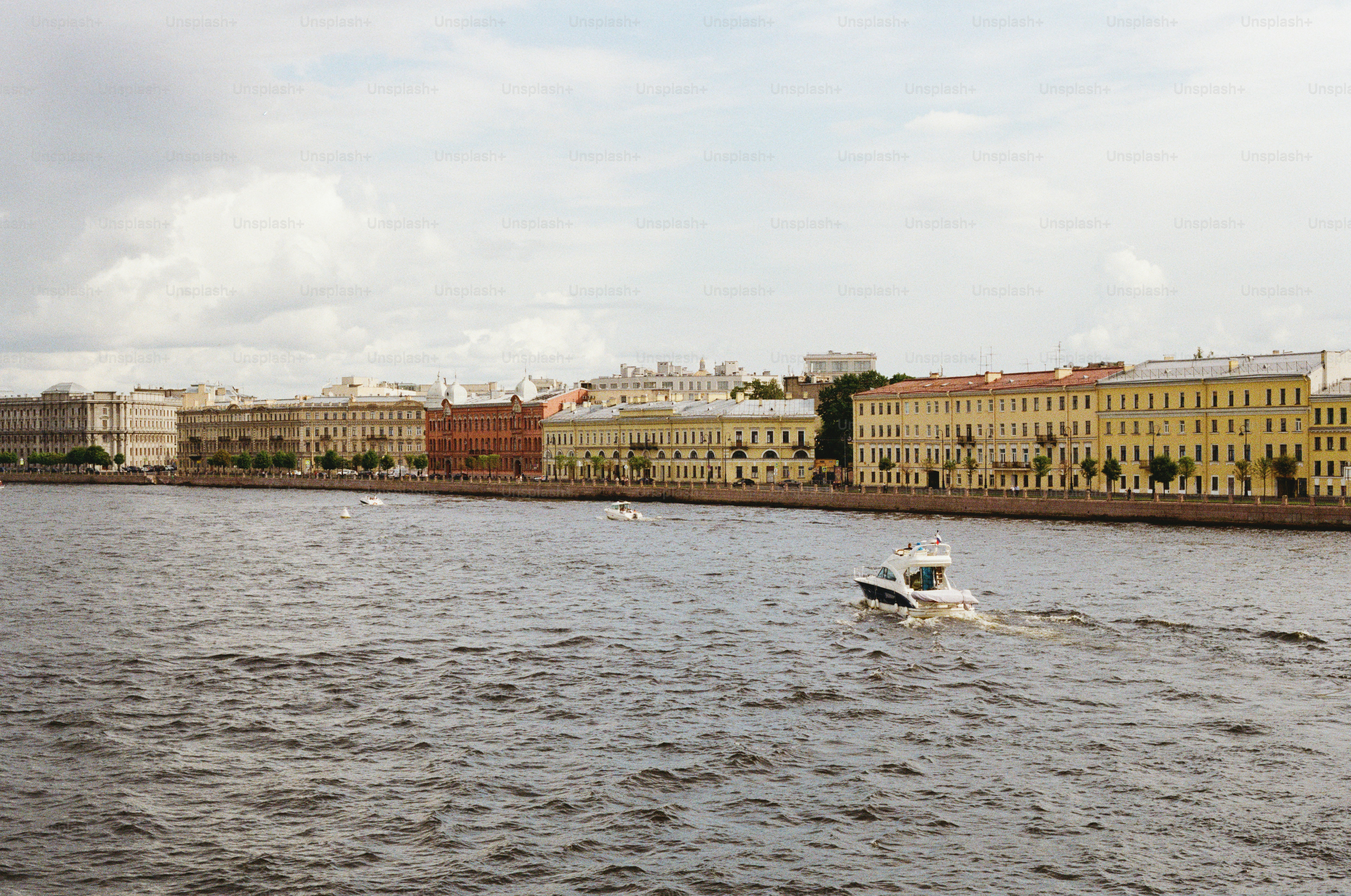 A boat travels on a wide river with buildings in the background