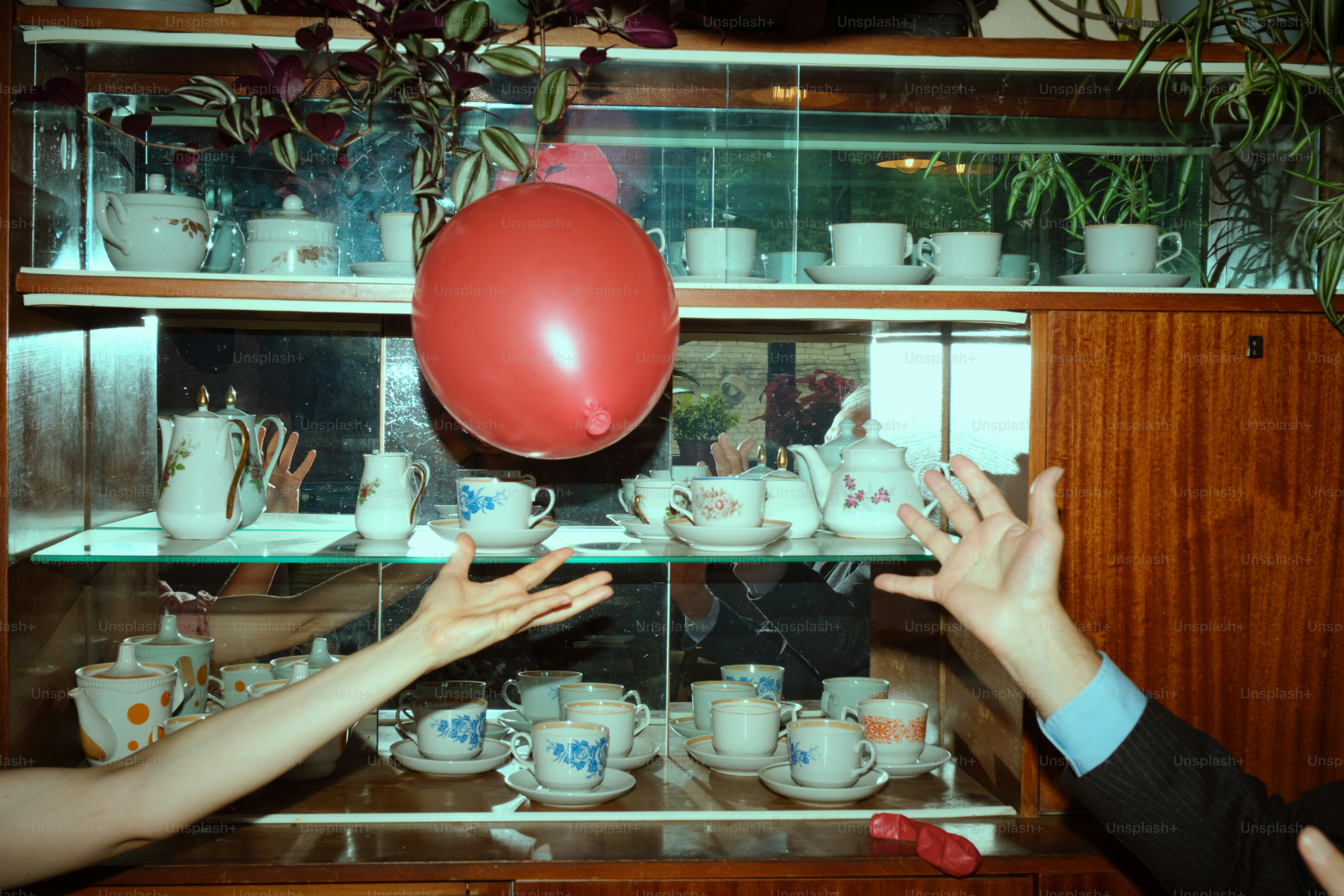 Red balloon floats between two hands near cabinet