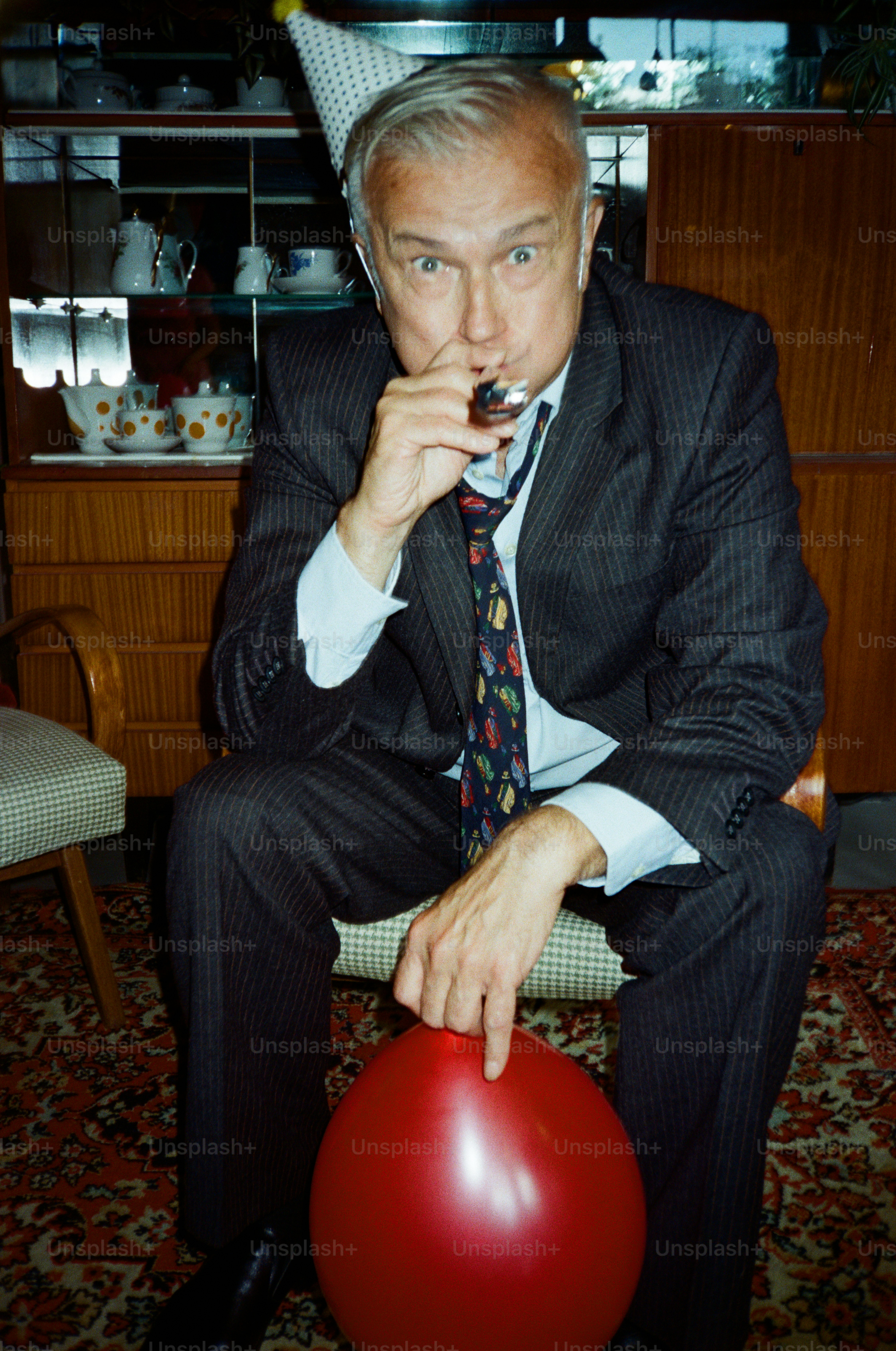 Man in suit with party hat blows party blower