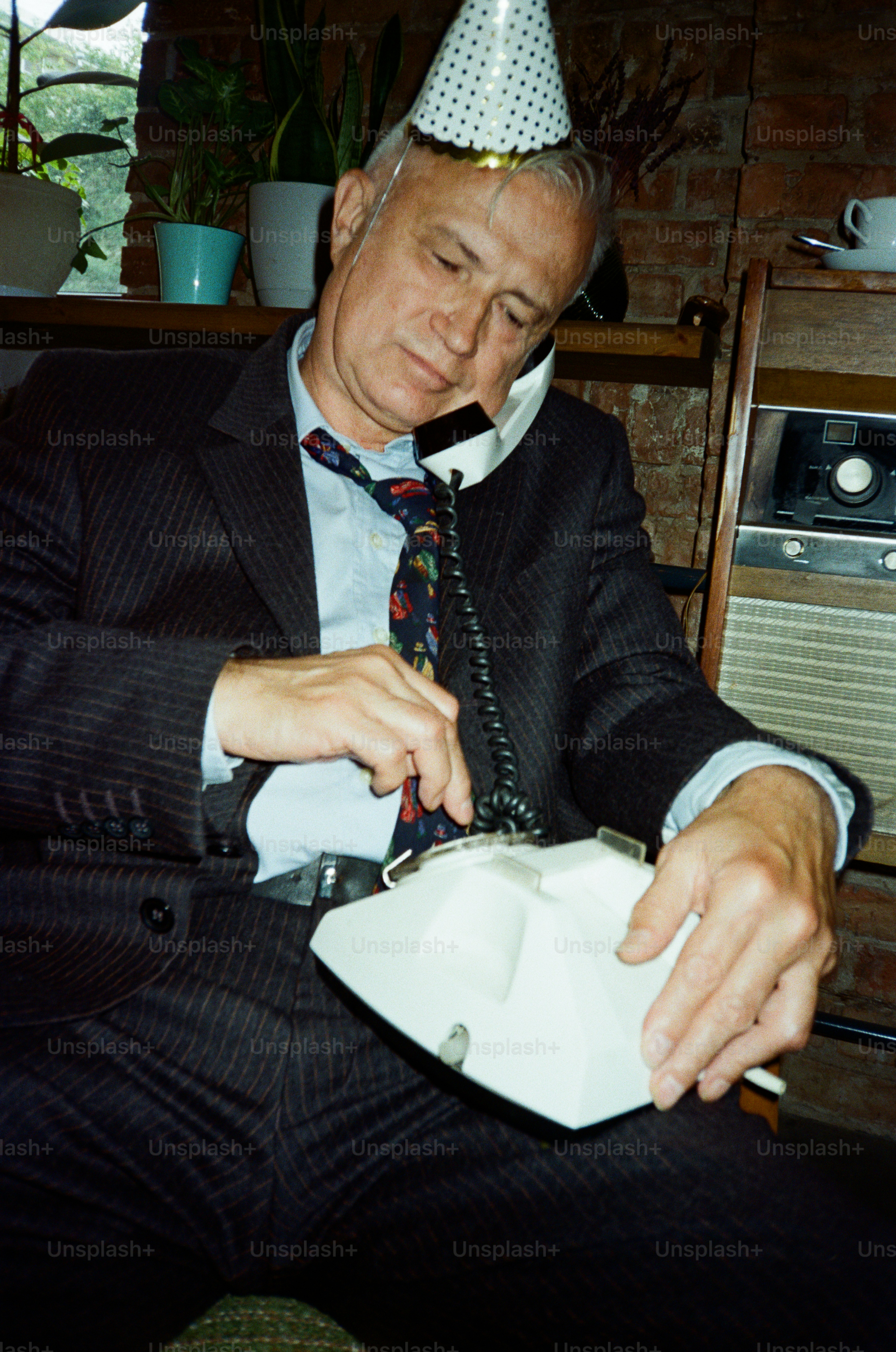 Man in party hat talks on old phone