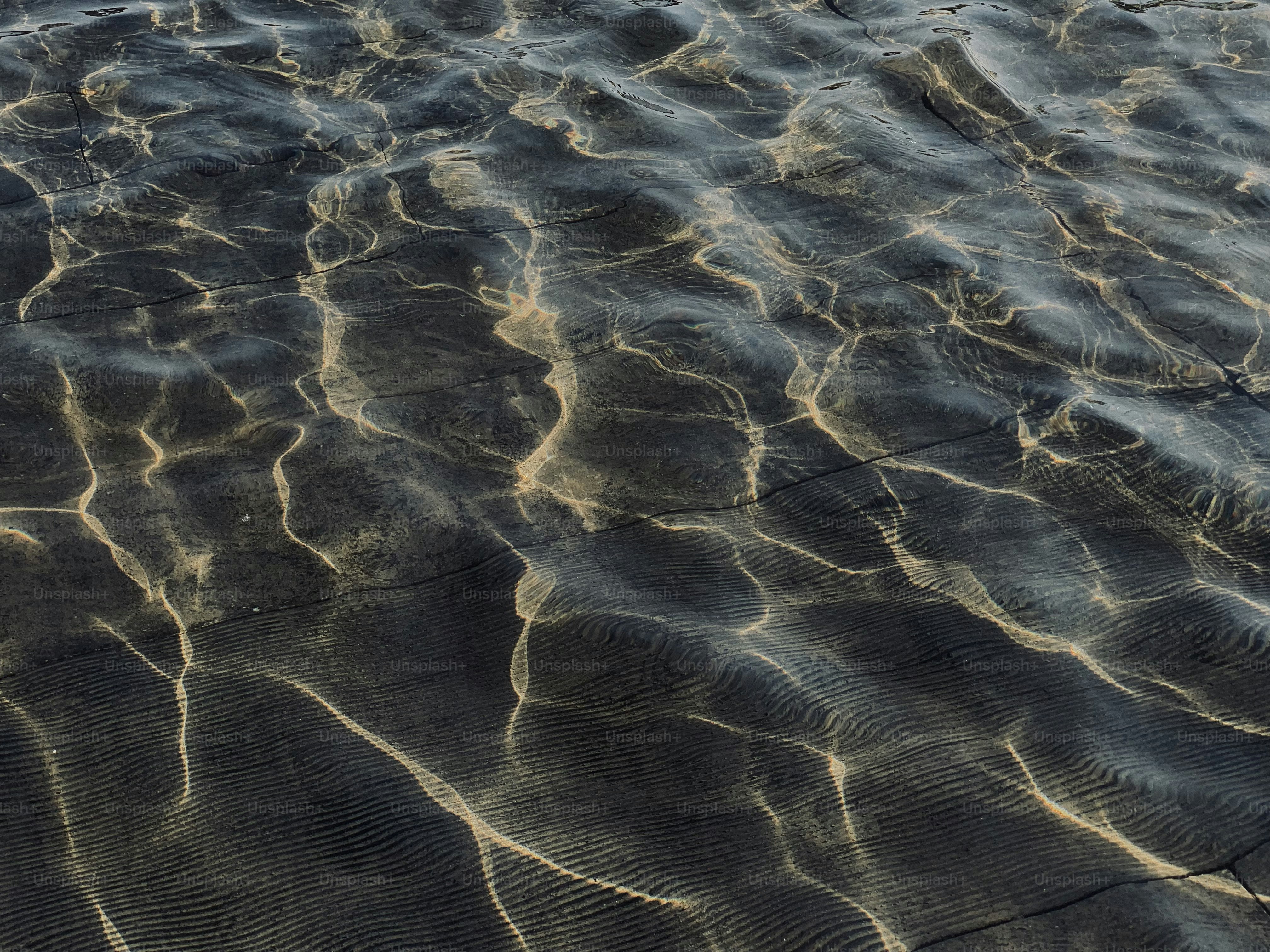 Rippling water surface with light reflections on sand.