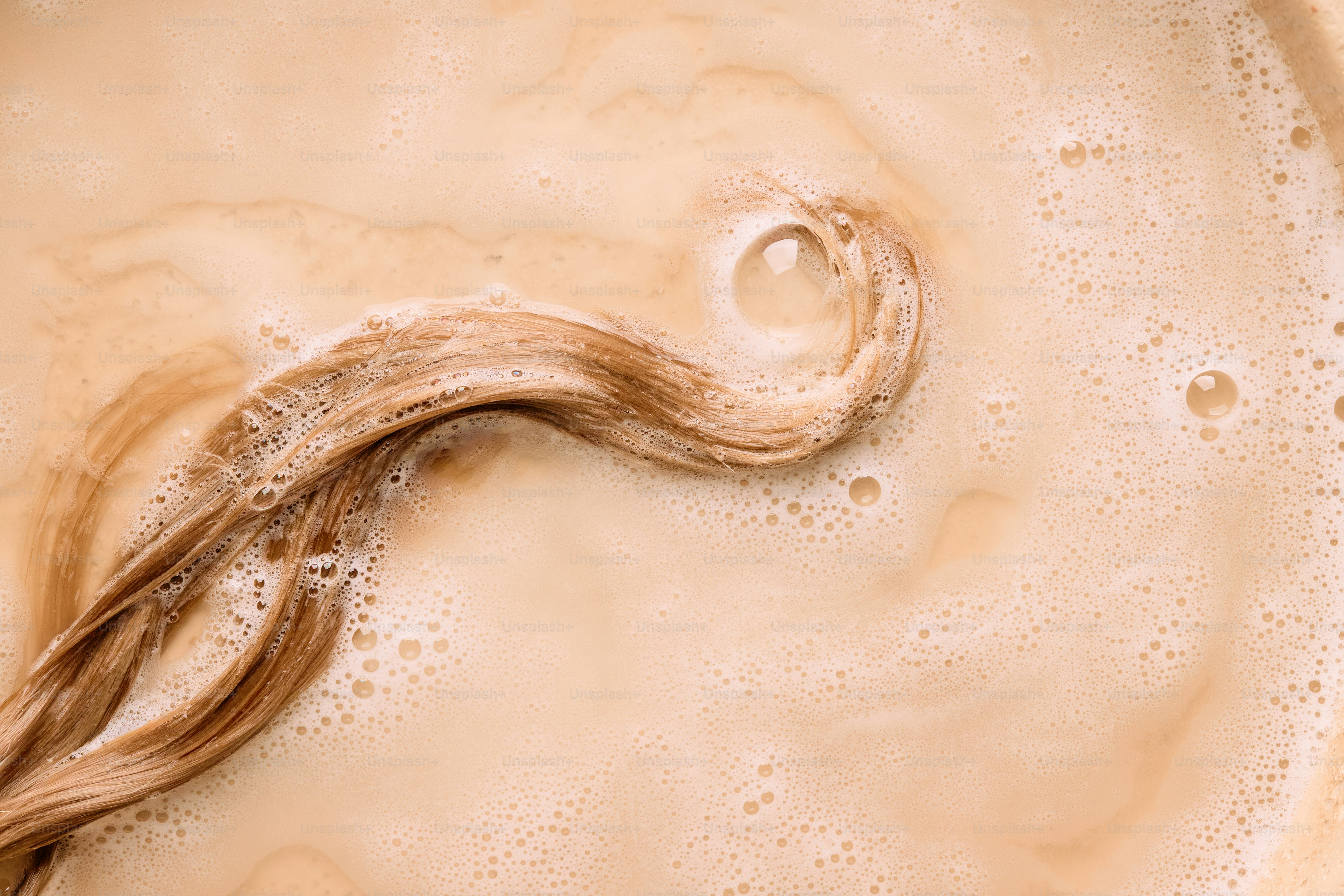Blonde hair strand swirling in creamy liquid