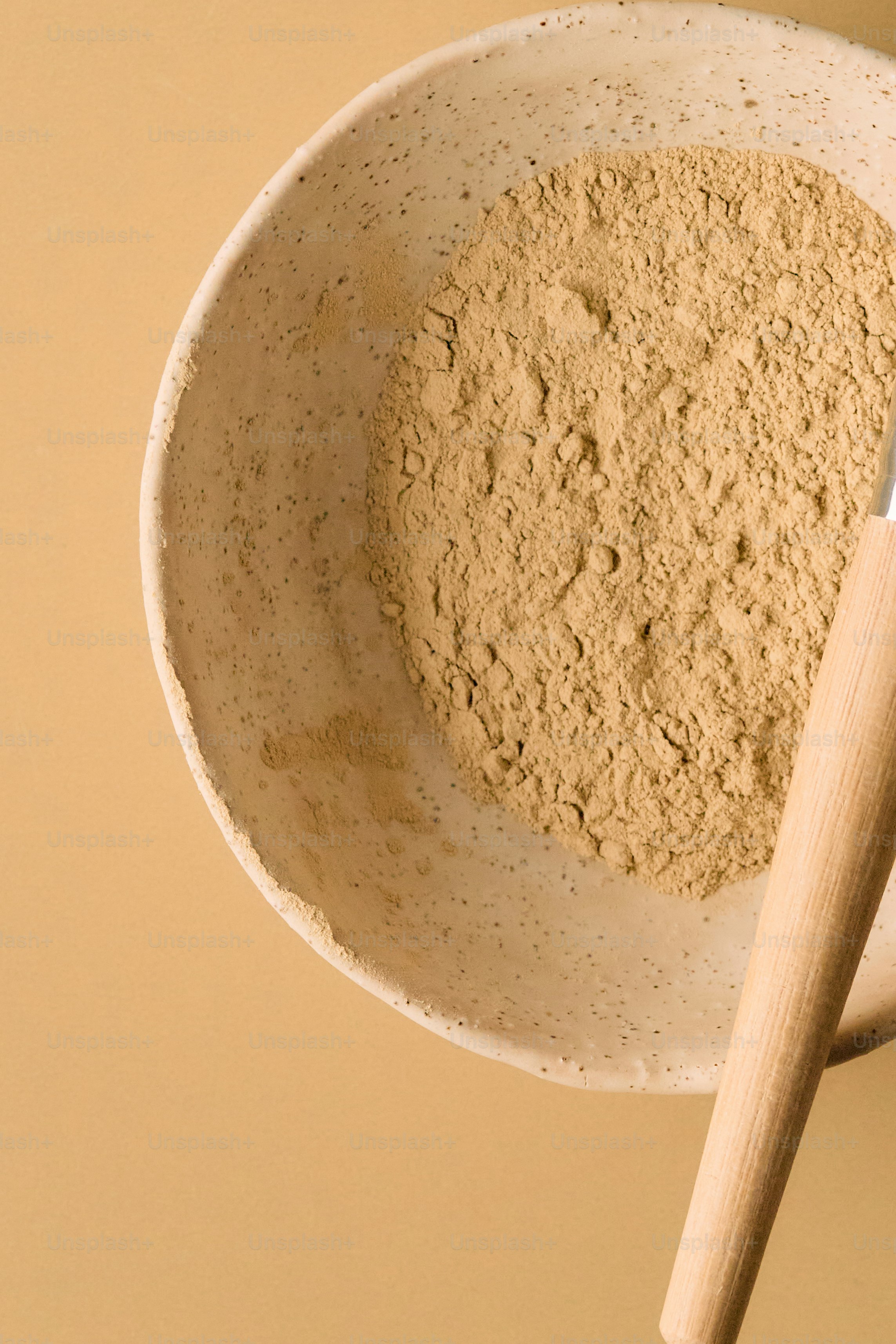 Bowl of tan powder with wooden applicator