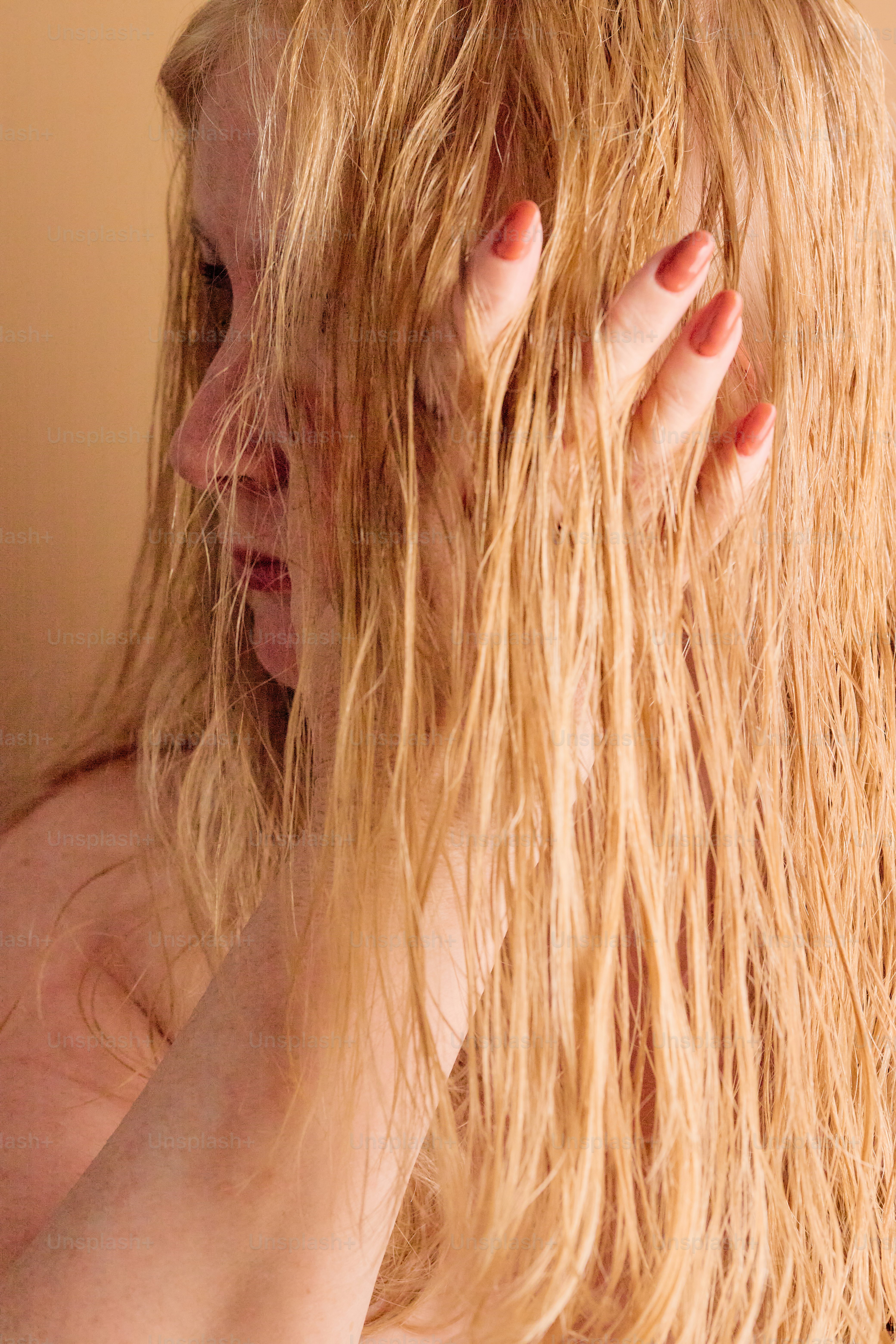Blonde Frau mit nassen Haaren, die ihr Gesicht berühren.