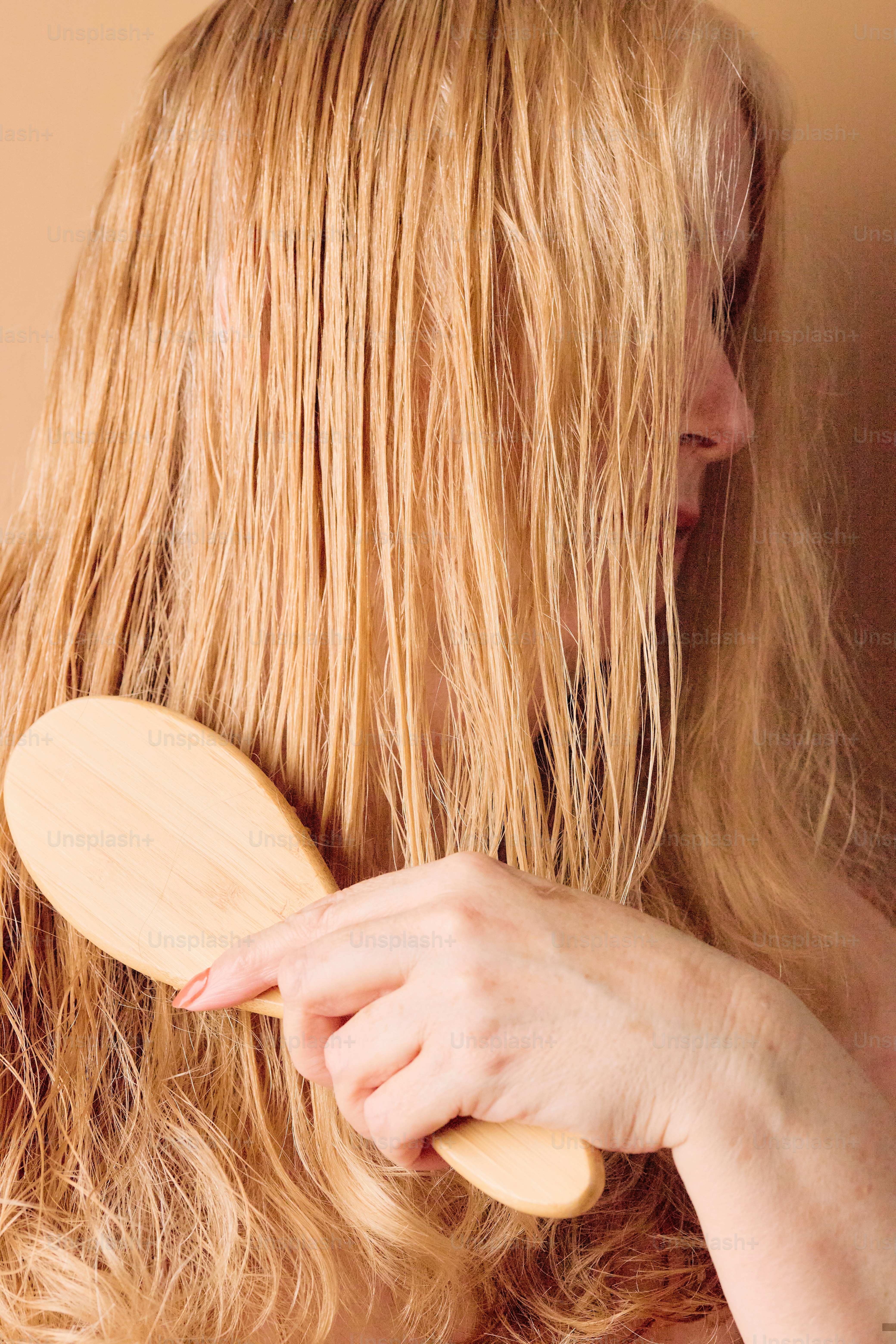 Frau bürstet nasses blondes Haar mit Holzbürste