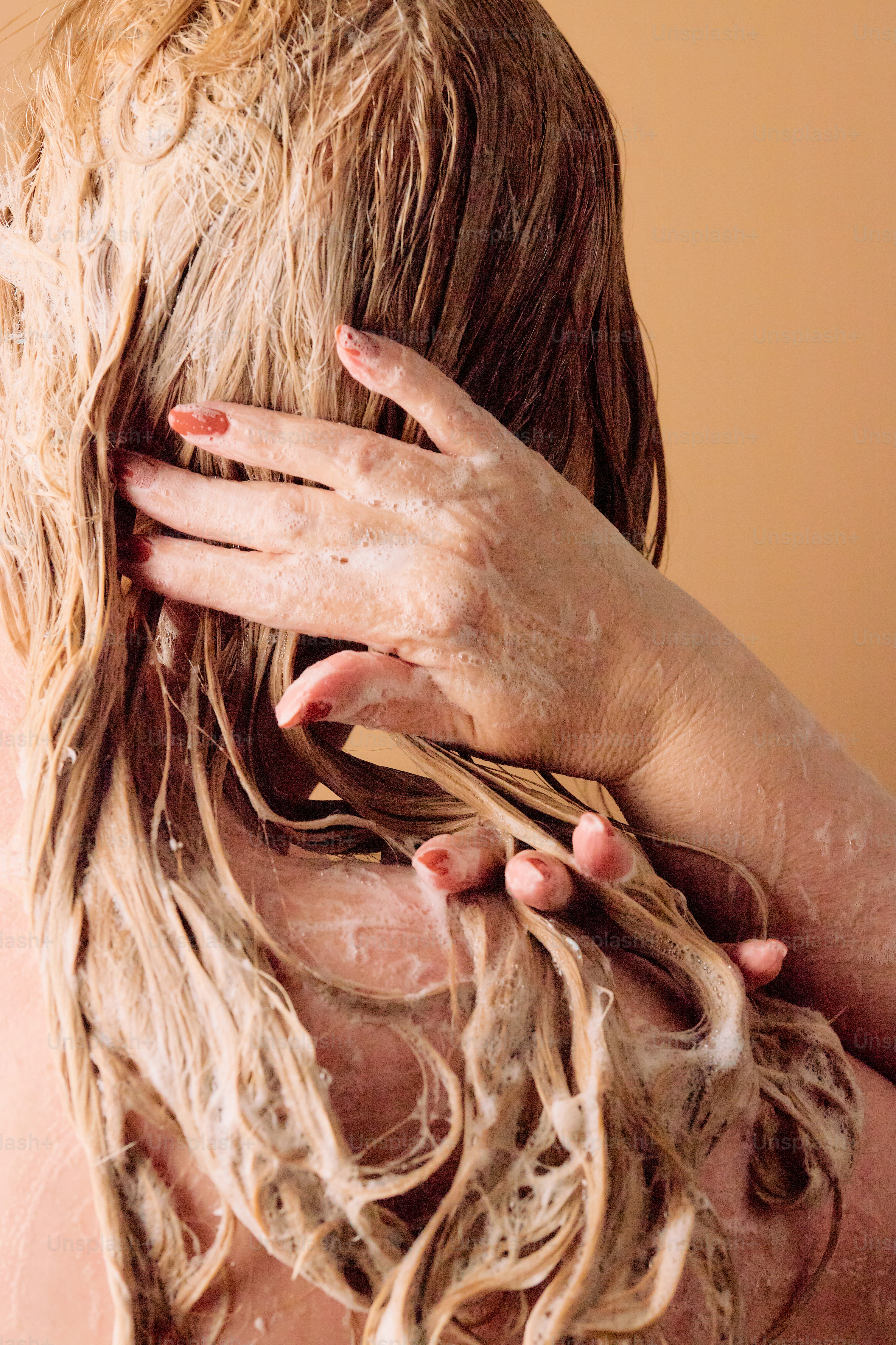 Frau, die blonde Haare mit Shampoo wäscht