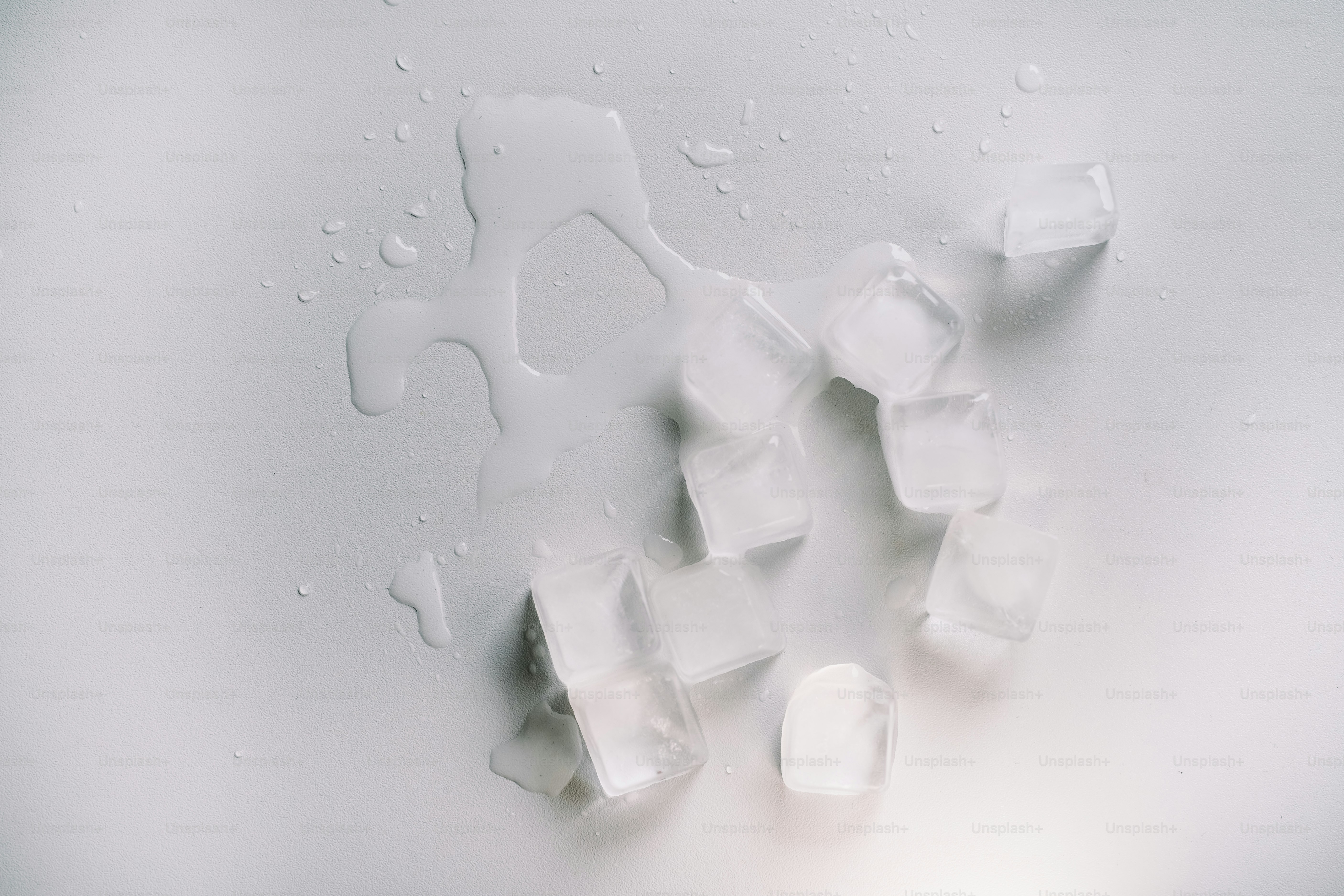 Overhead view of scattered ice cubes and melting water on a textured white surface, evoking a crisp, cold, and refreshing atmosphere.