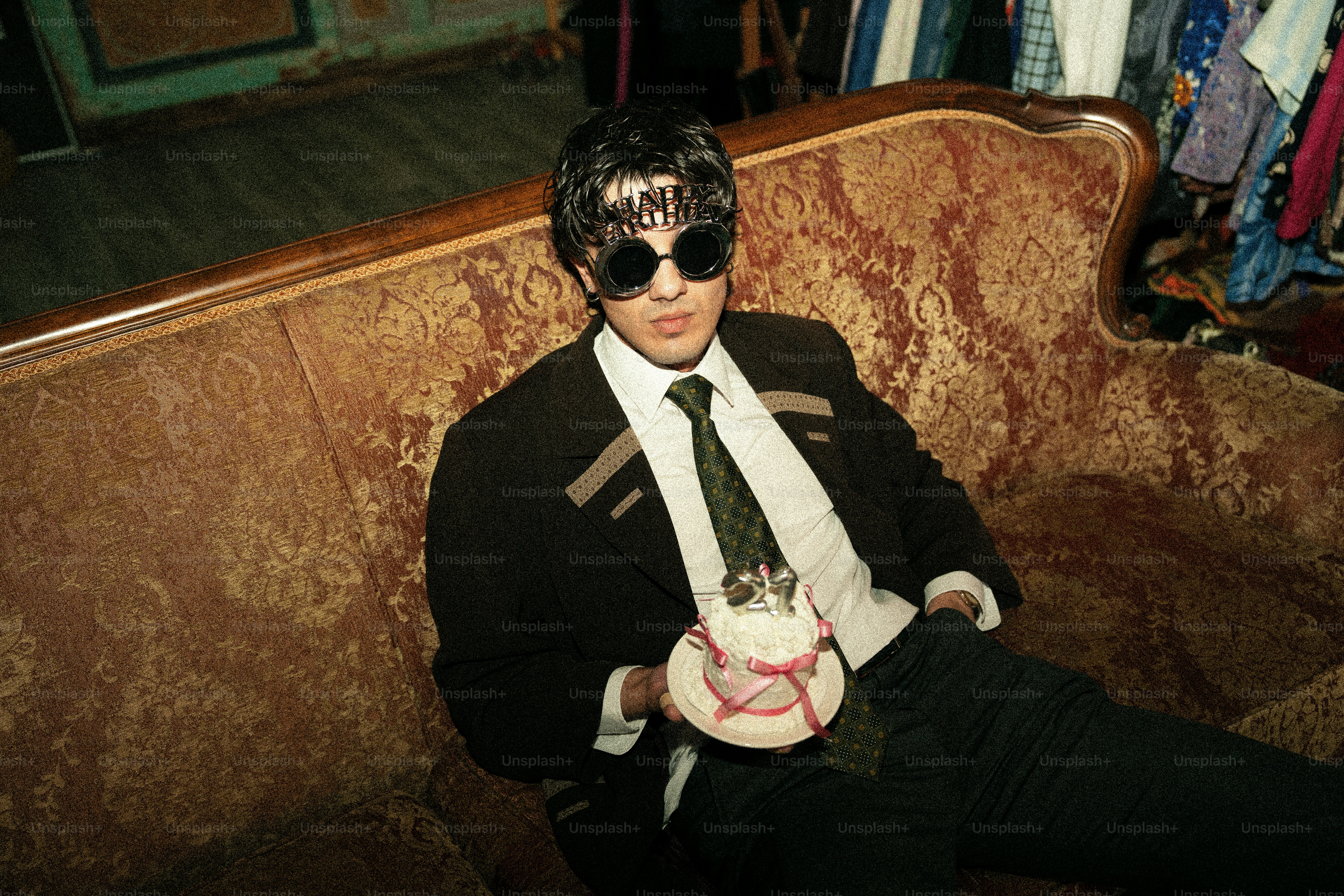 Man in sunglasses and suit sits on couch with cake