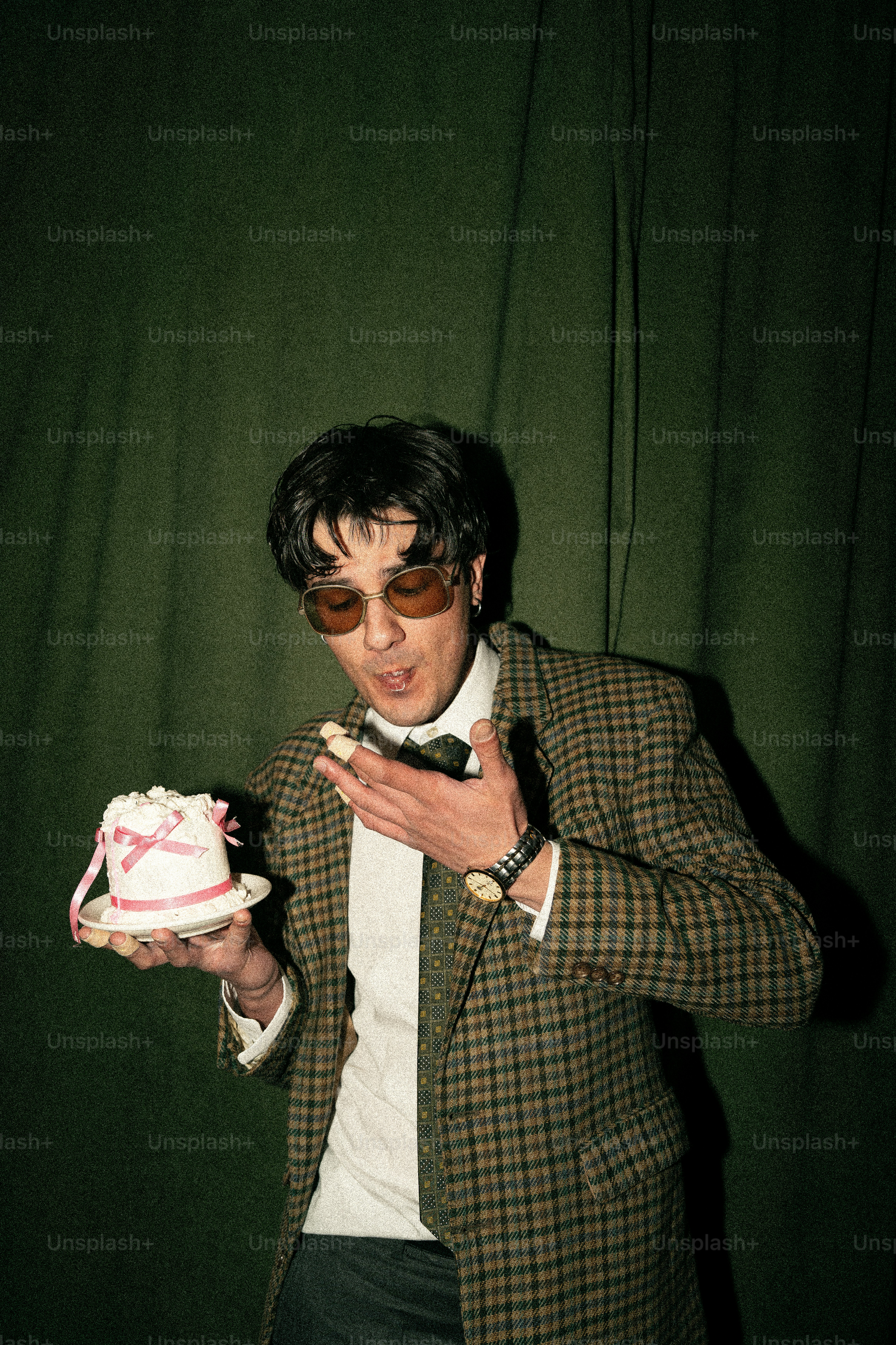 Man in suit holding a small cake with pink ribbon.
