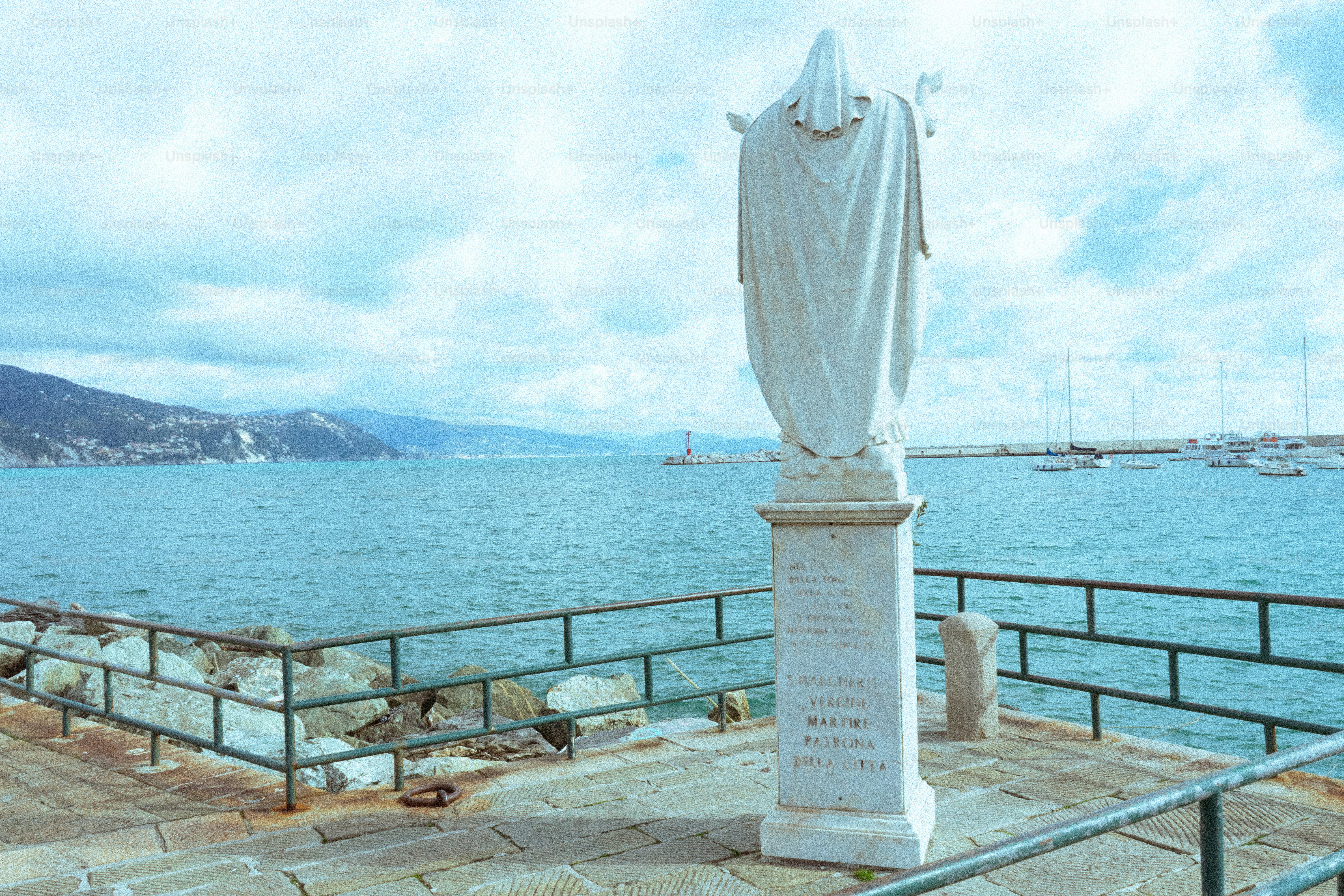 White statue overlooking the ocean with sailboats