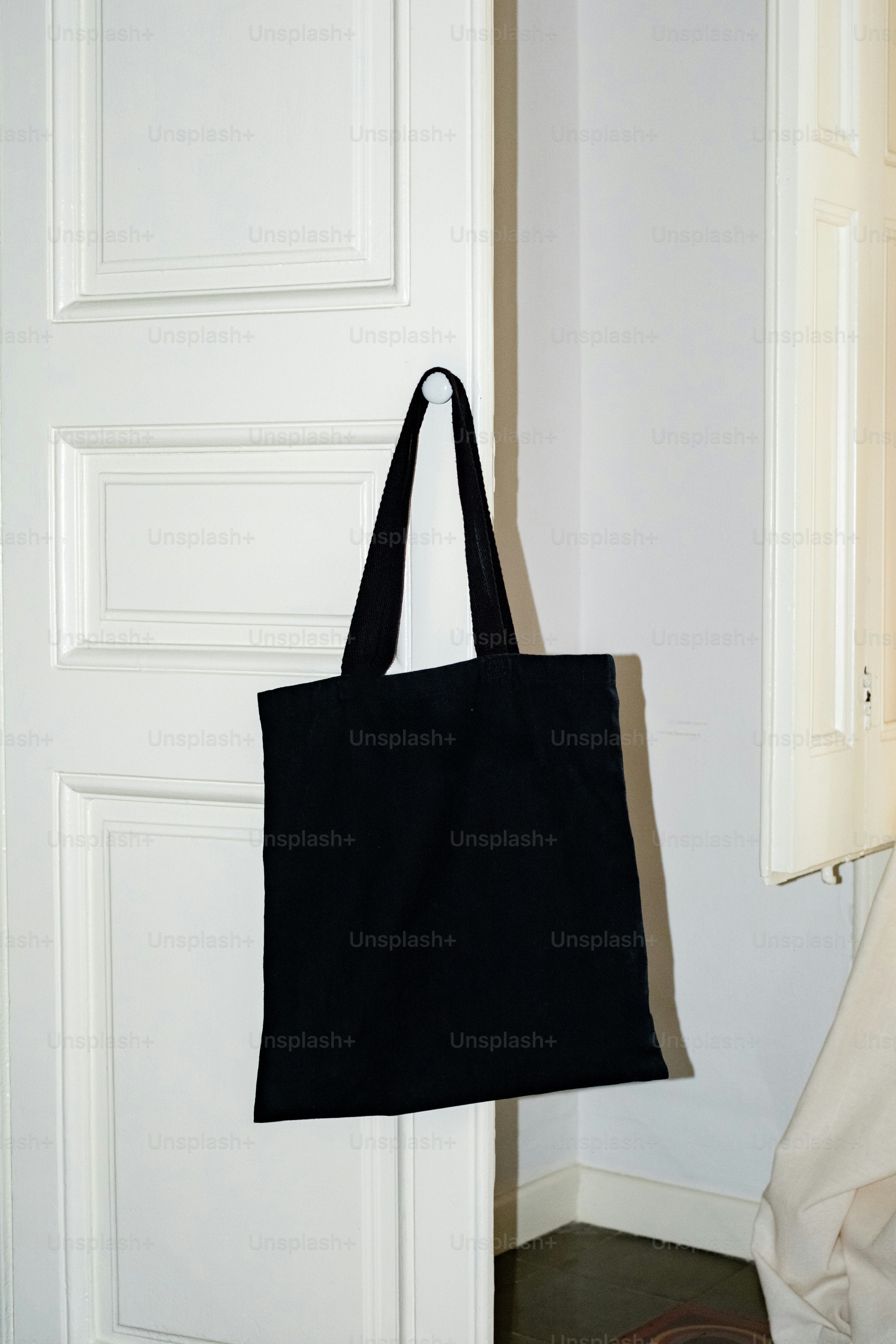 Un sac fourre-tout noir est accroché à une patère de porte blanche.