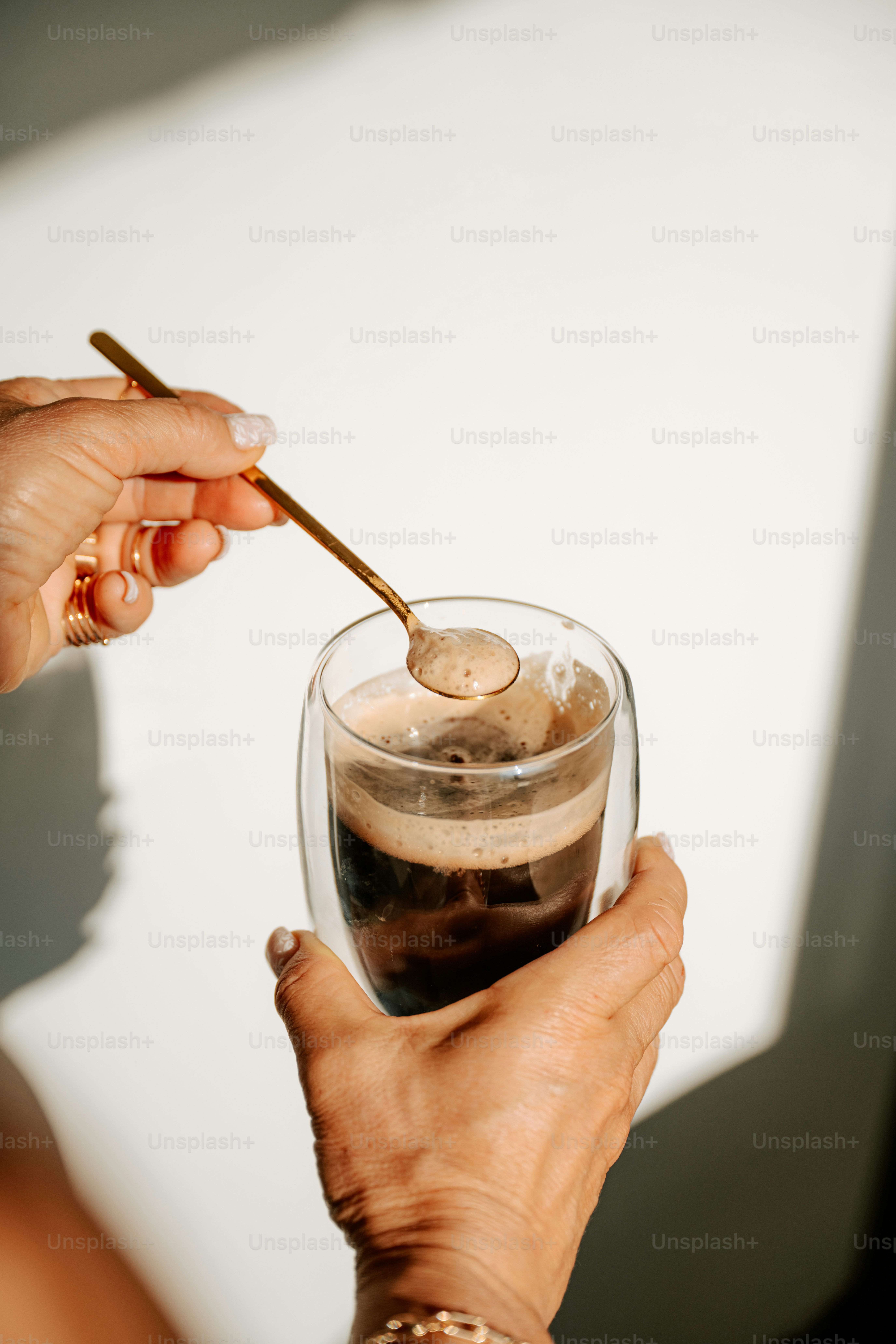 Hands stirring a glass of dark coffee with a spoon