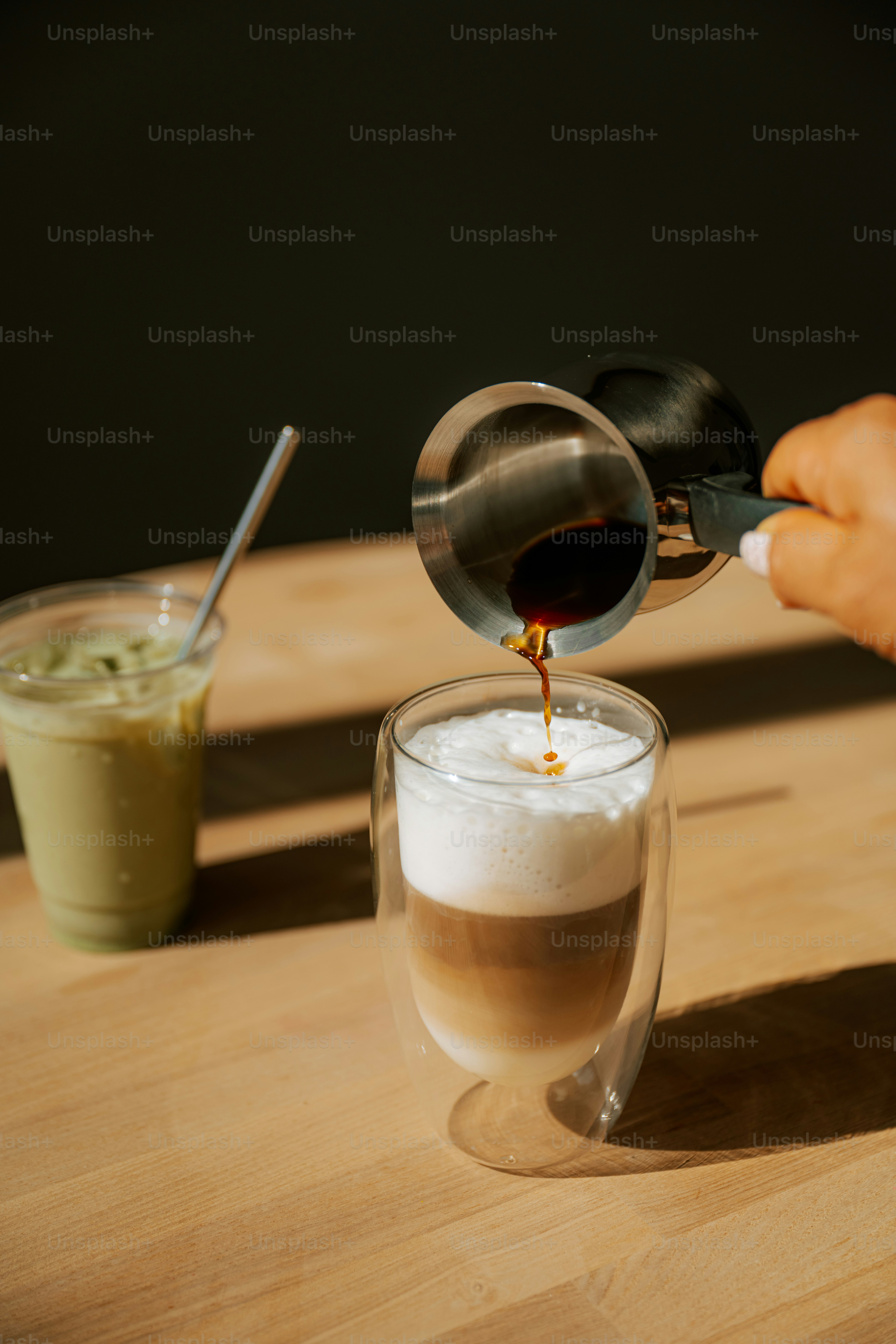 Pouring coffee into a layered latte with iced matcha.