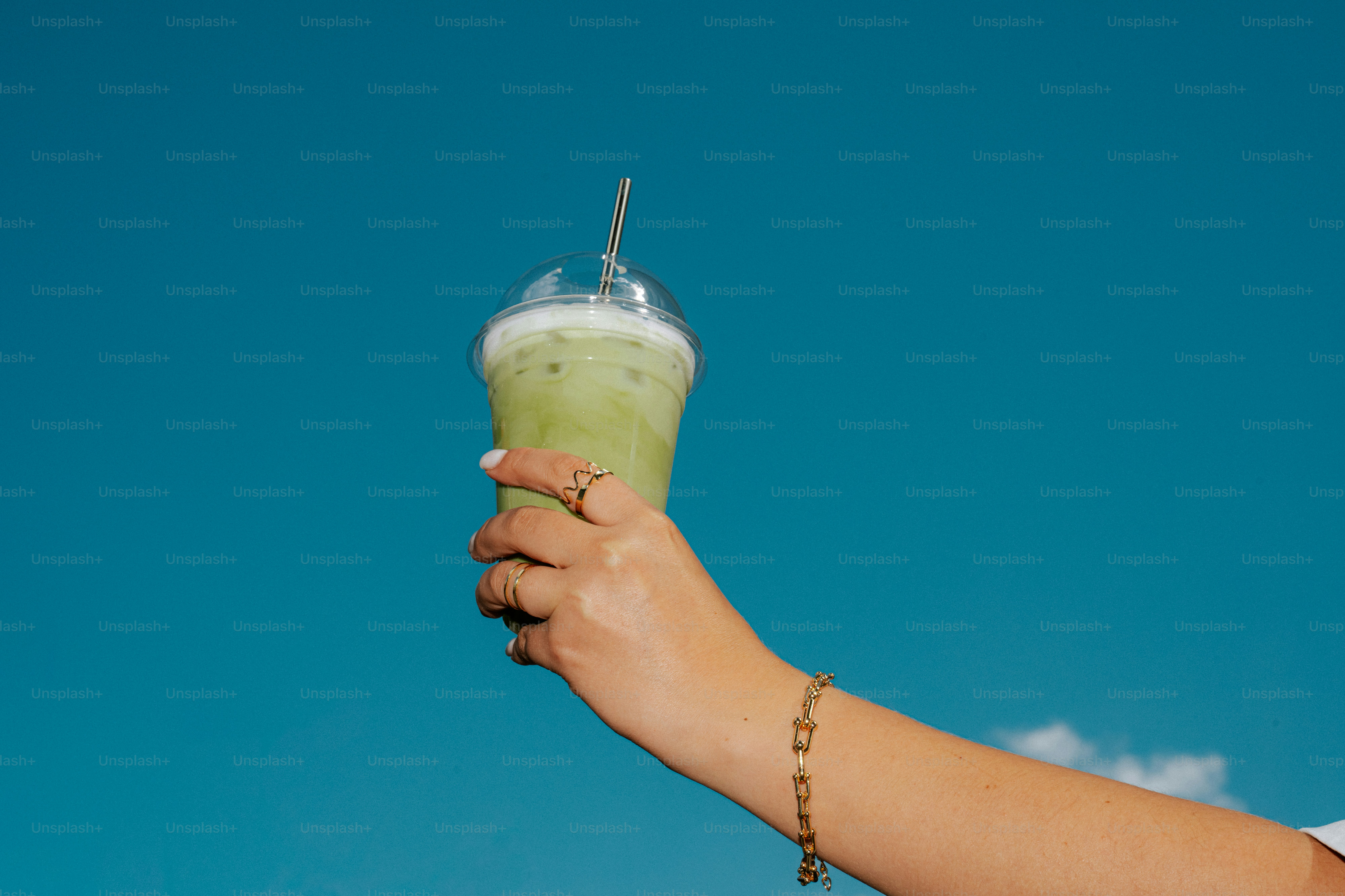 Hand holding a green drink against blue sky