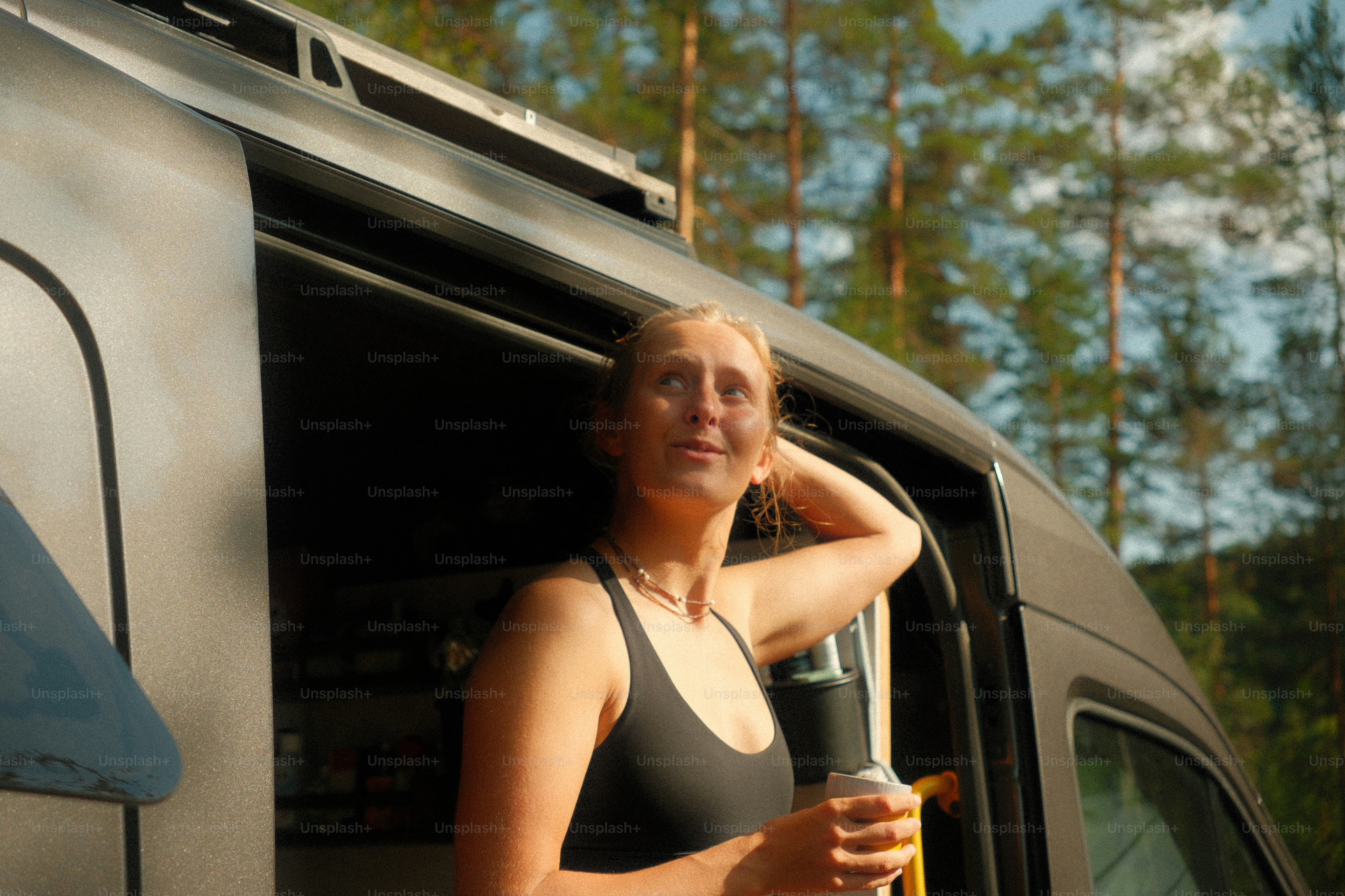 Woman holding drink by van in sunny forest