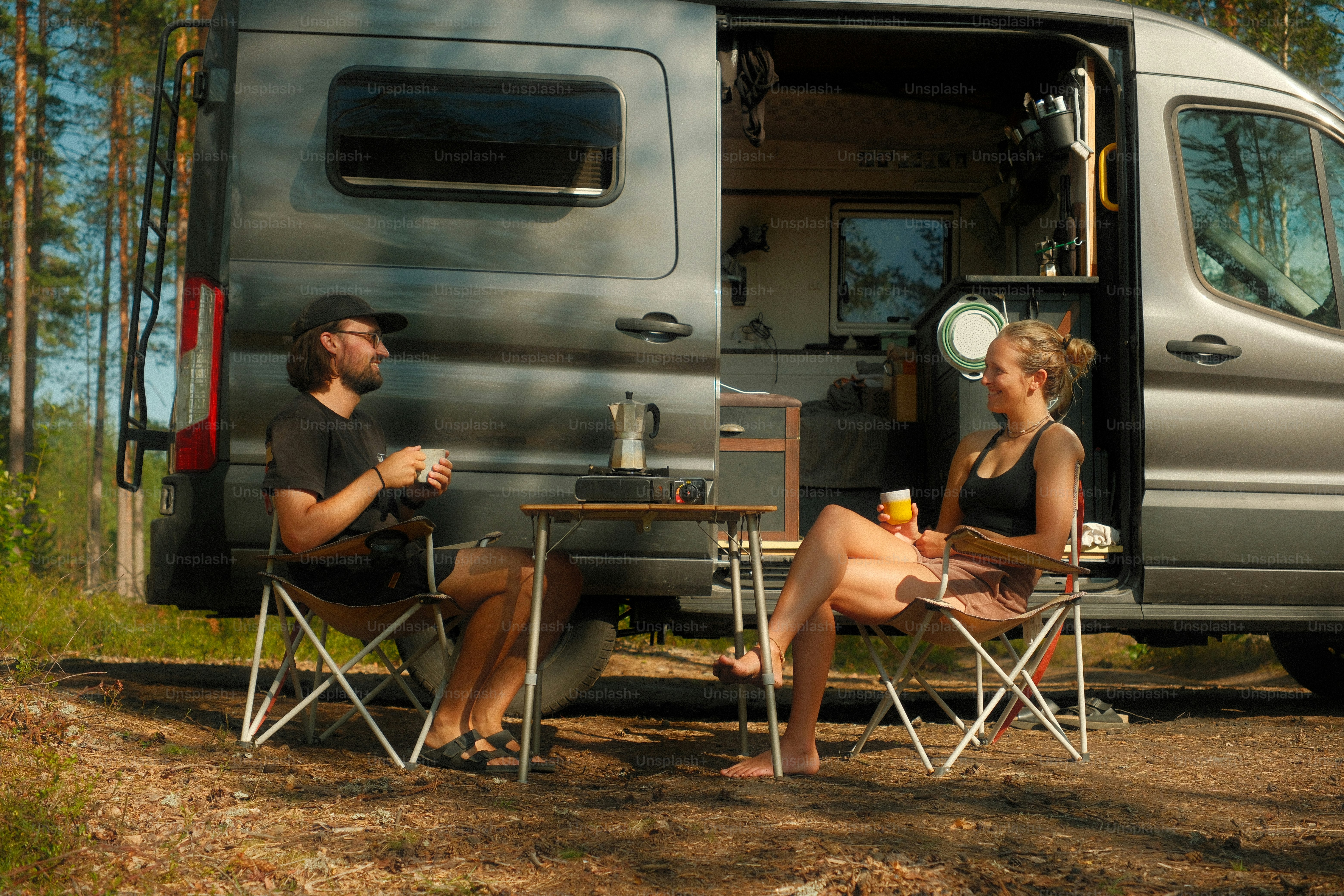 Couple enjoying drinks by a camper van in forest