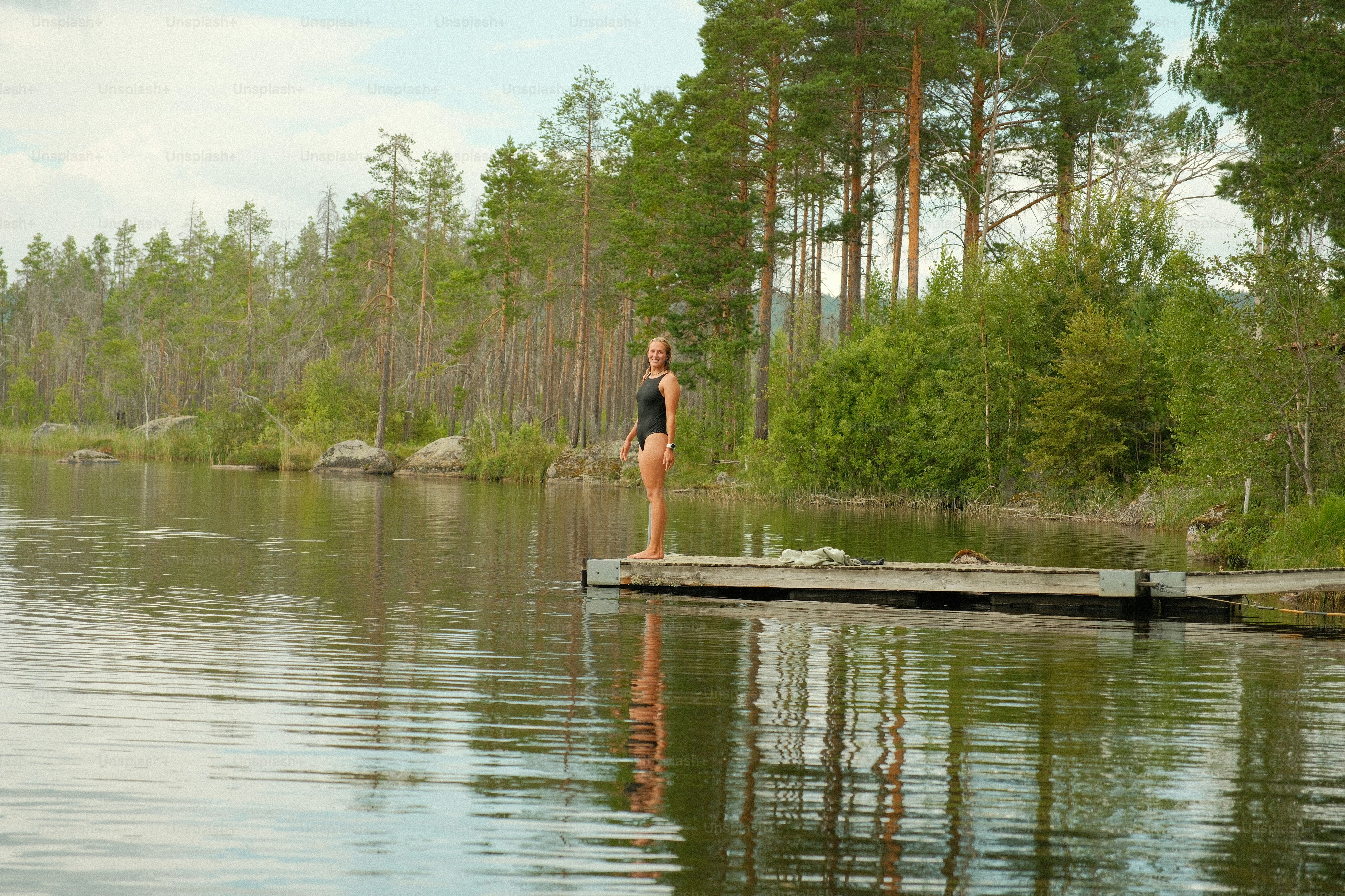 Woman in swimsuit stands on dock by lake