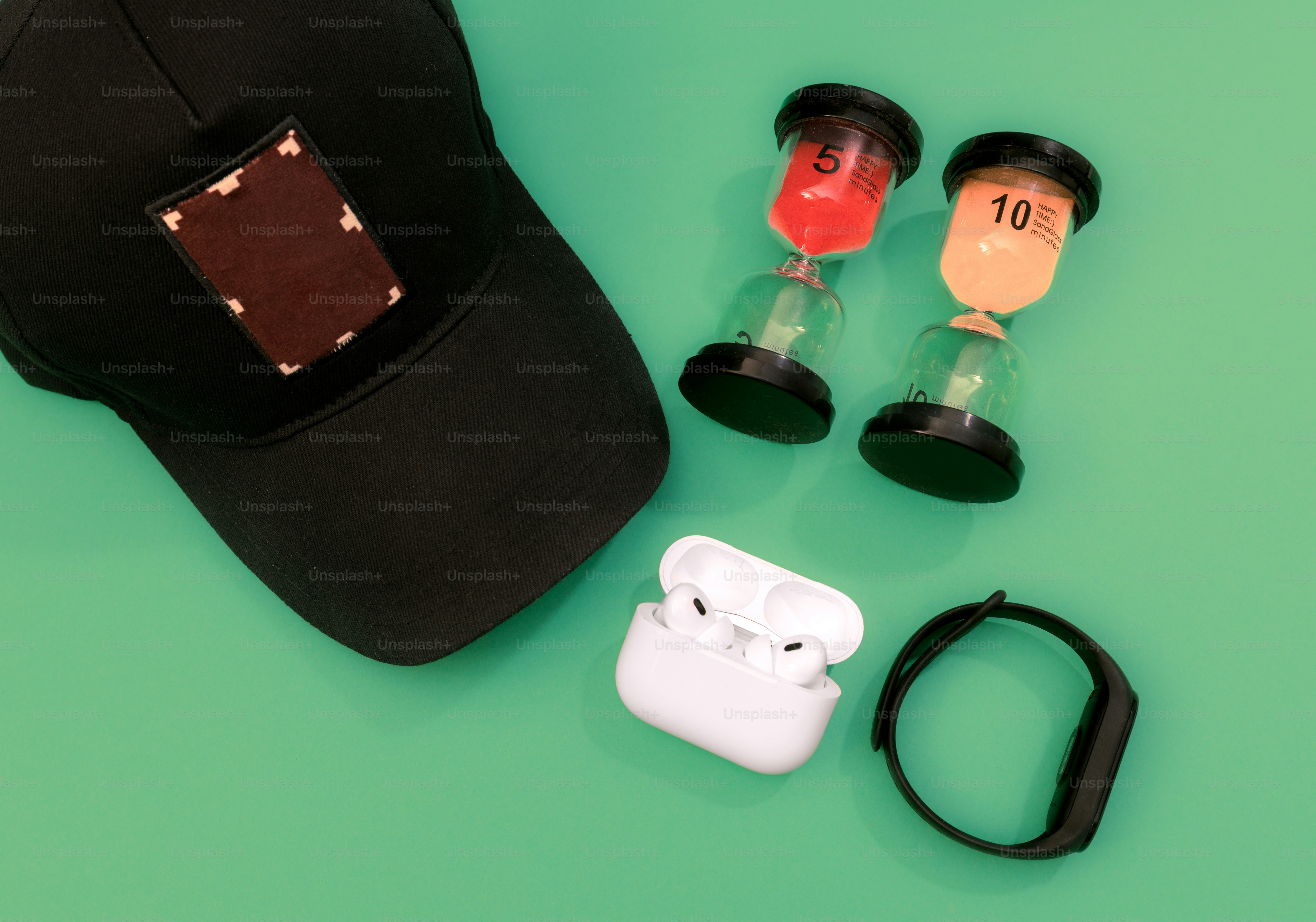 Black cap, earbuds, smartwatch, and hourglass timers on green background