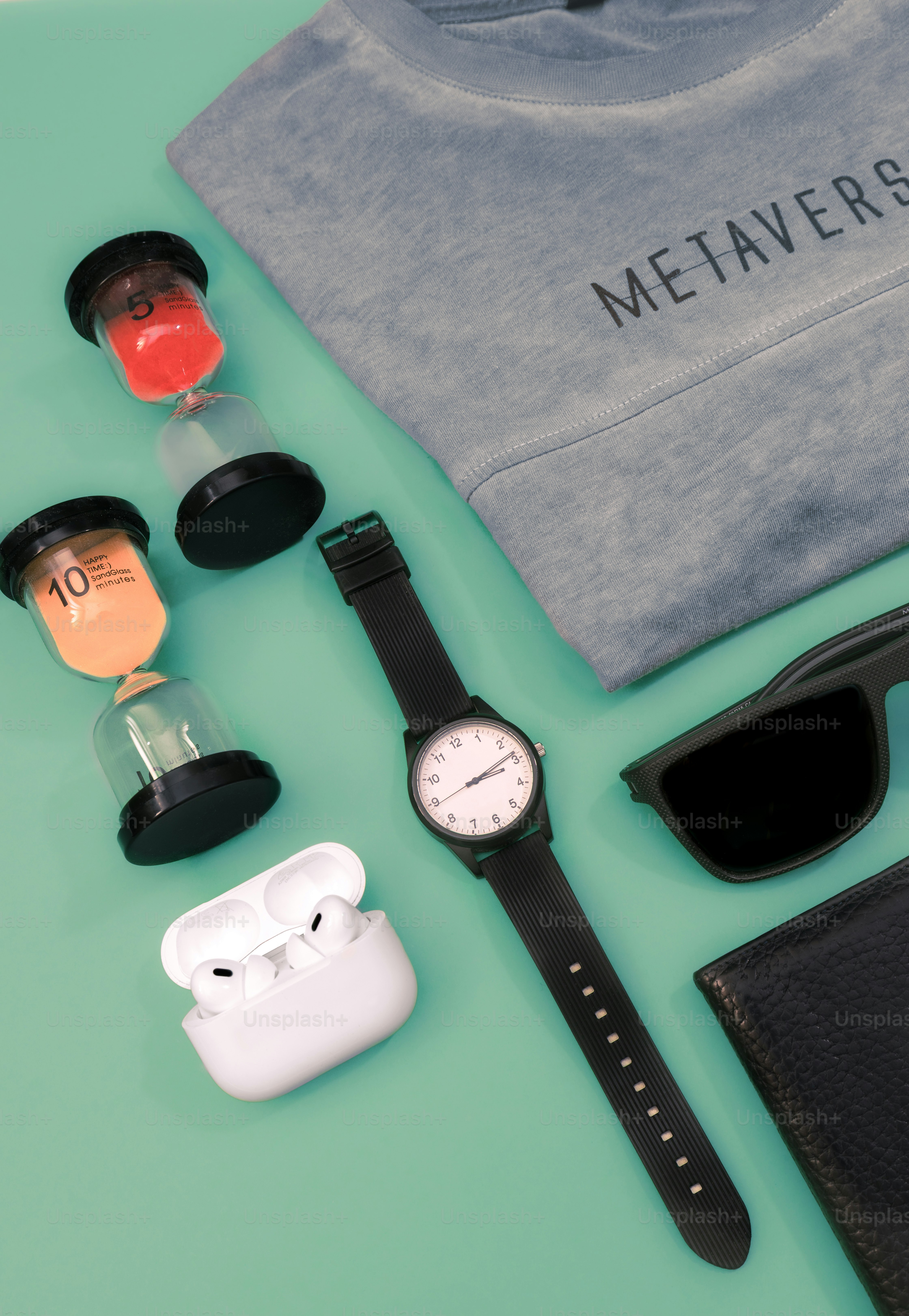 Gray sweatshirt, watch, sunglasses, earbuds, and hourglasses and wallet on green