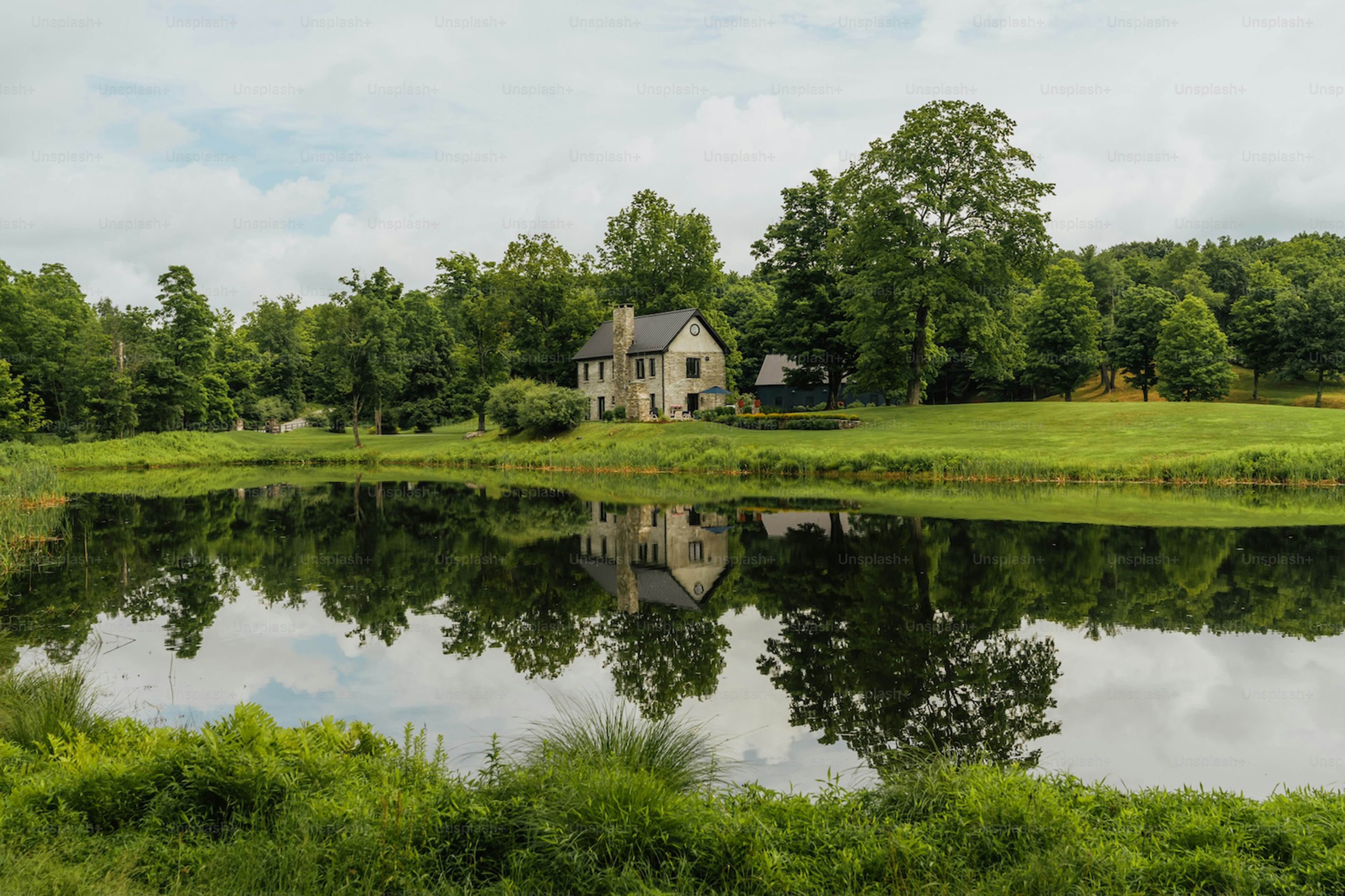 Stone house reflected in a calm lake surrounded by trees.